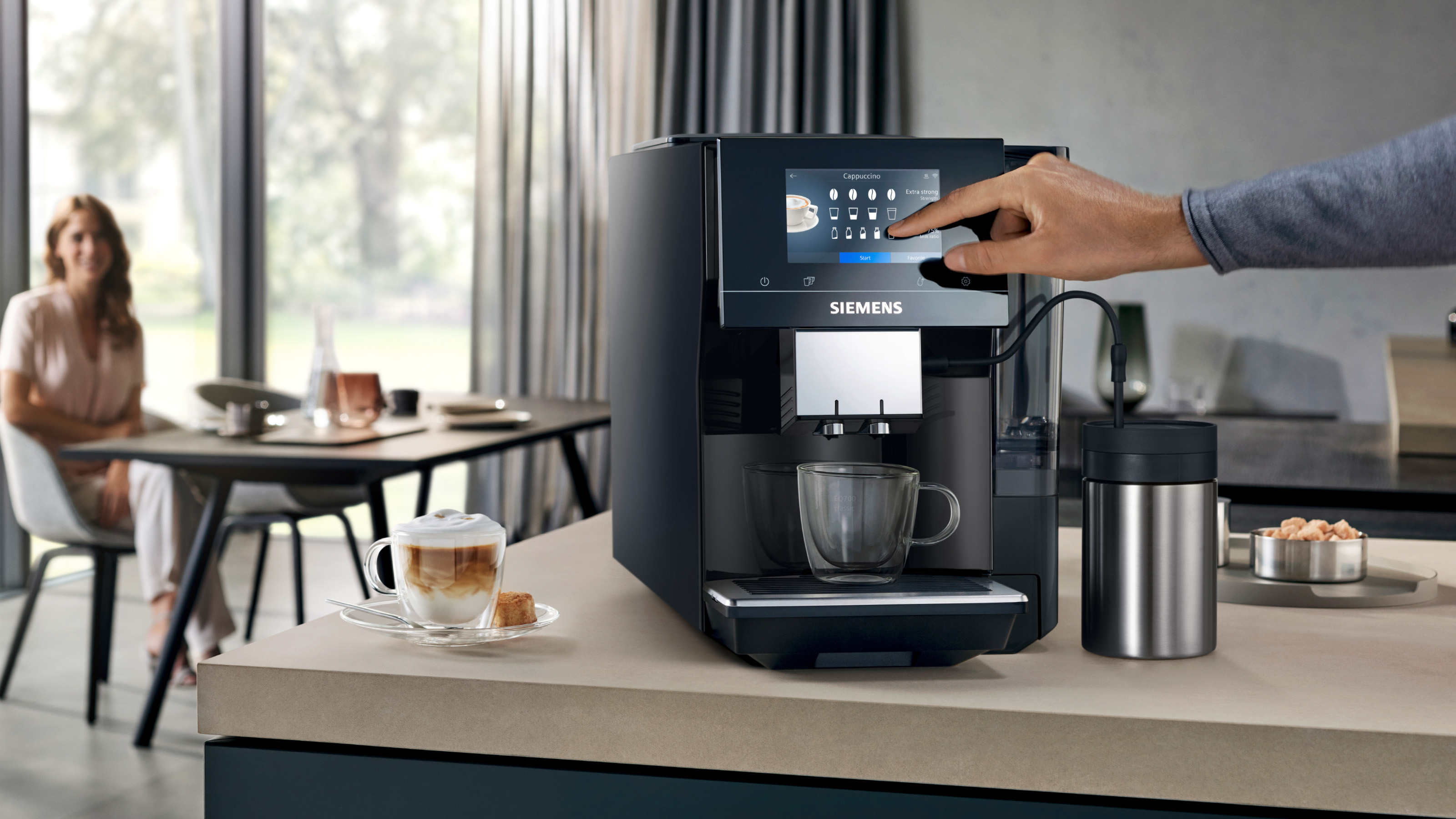 Eine Person benutzt eine schwarze Kaffeemaschine mit Touchscreen. Eine Tasse ist für Kaffee platziert.