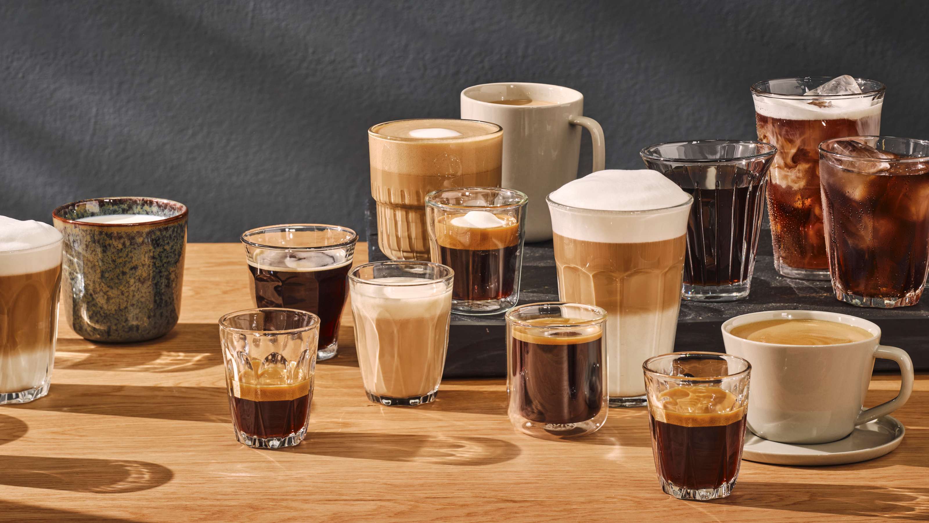 Viele Kaffeegetränke in Gläsern und Tassen, mit Schaum und verschiedenen Farben, alles auf Holz.