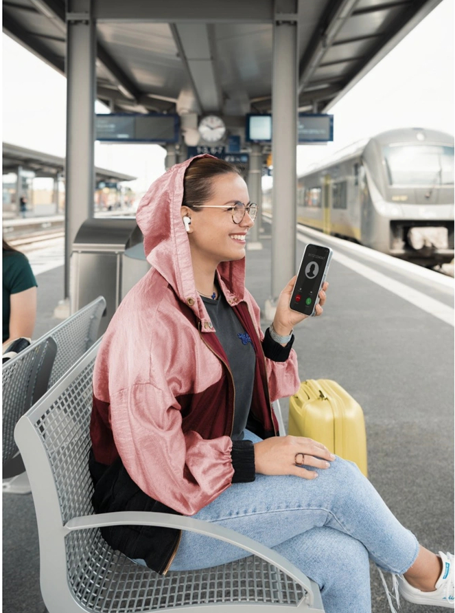 Kobieta siedząca na stacji kolejowej, uśmiechająca się podczas rozmowy telefonicznej.