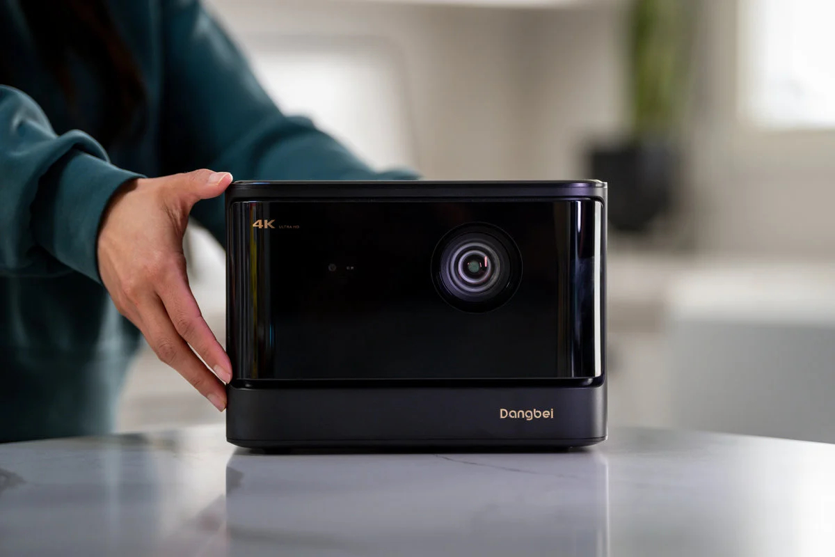 Czarny projektor z obiektywem i ręką osoby.