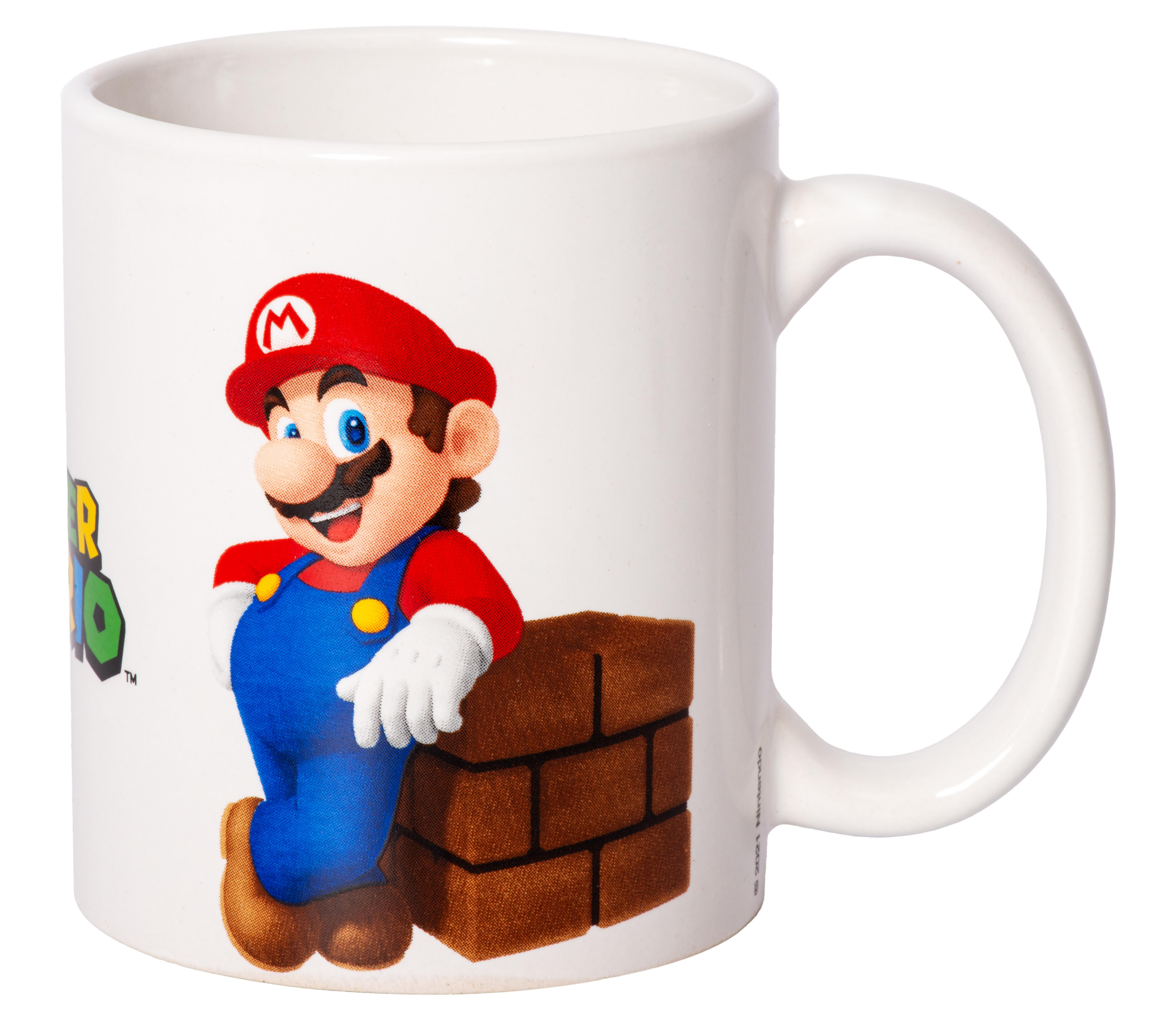Weiße Tasse mit einem lächelnden Mario-Motiv, das sich an eine Ziegelmauer lehnt. Henkel sichtbar.