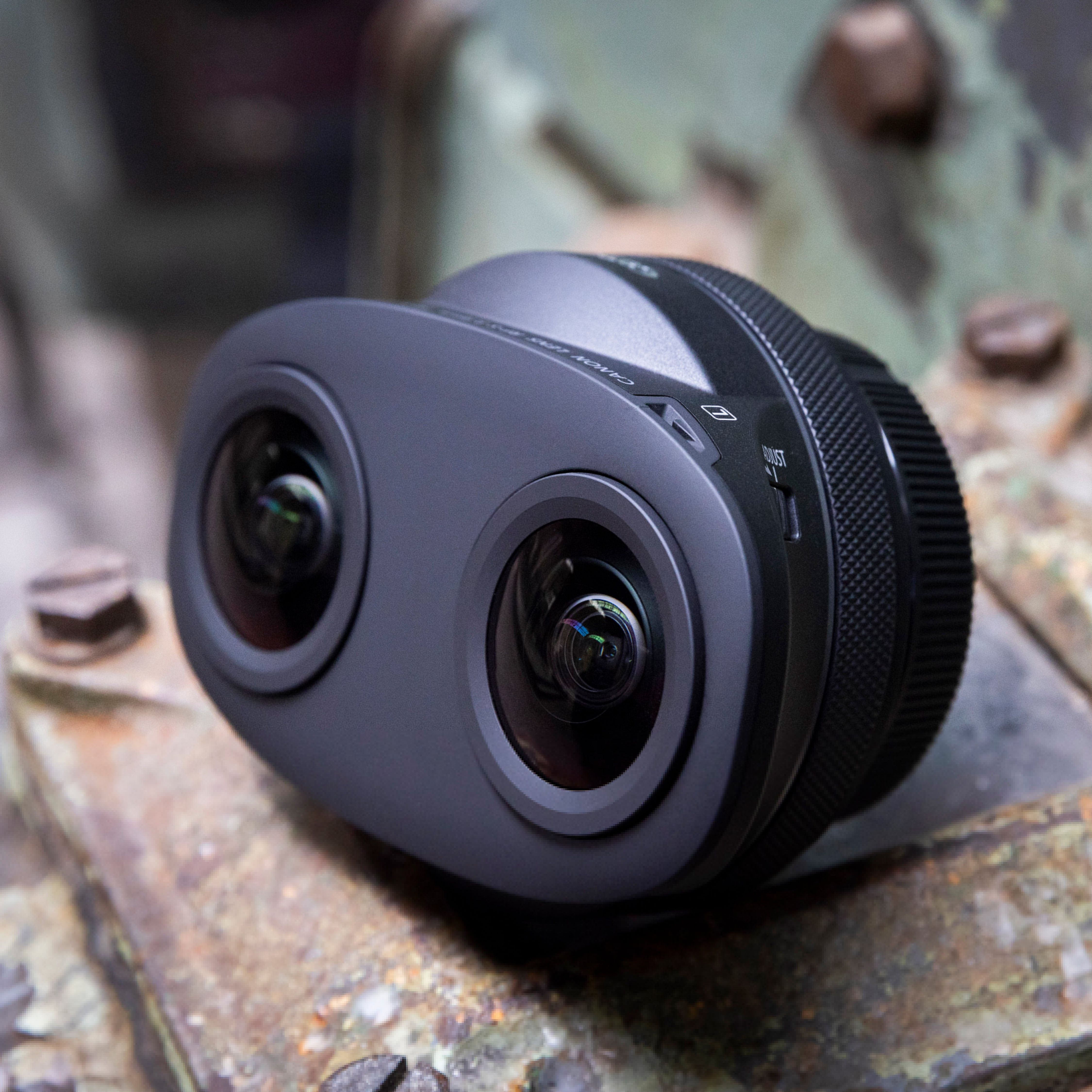 Una fotocamera VR Canon grigia a 360 gradi con due obiettivi è appoggiata su una superficie metallica arrugginita.