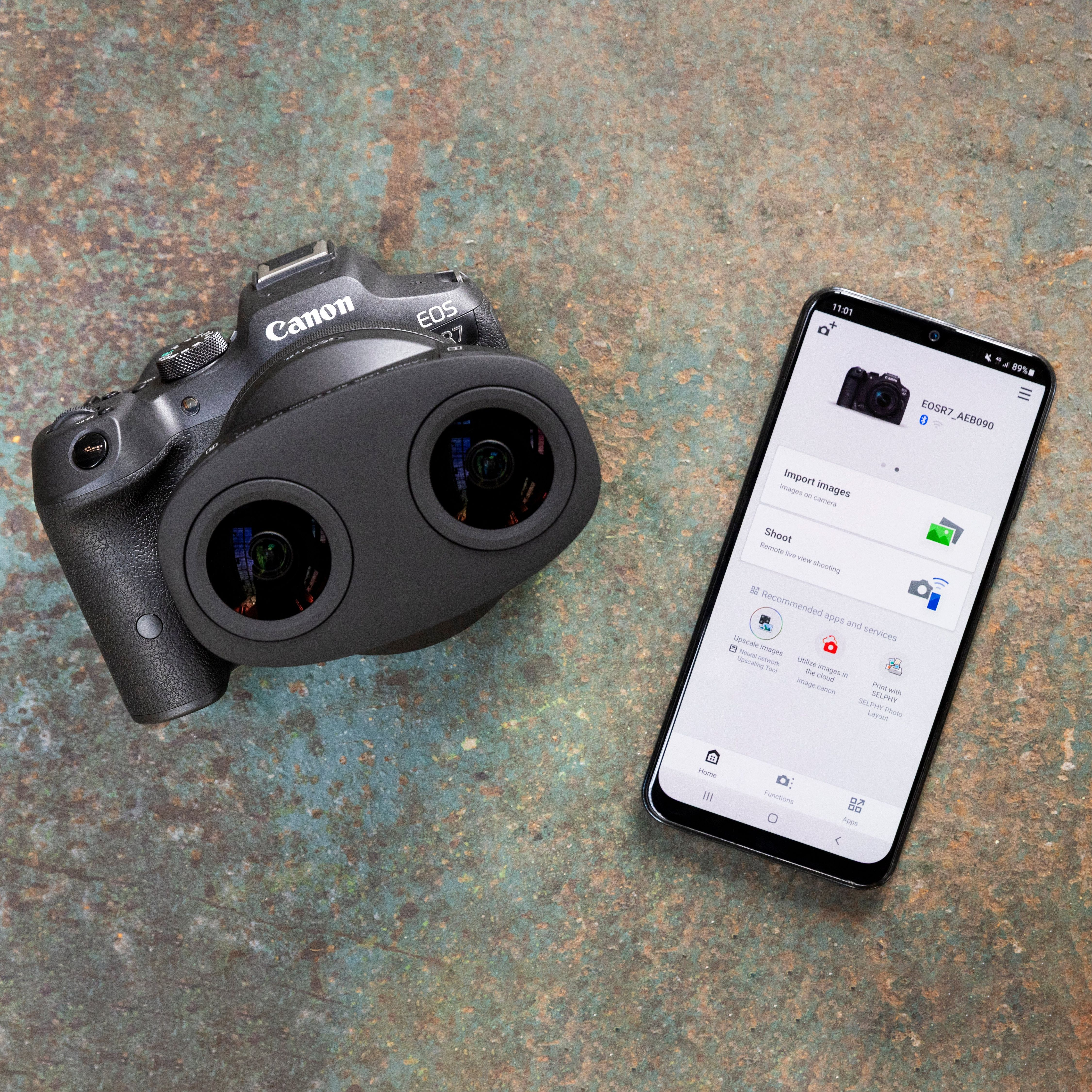 Una fotocamera Canon EOS R7 nera giace accanto a uno smartphone che mostra l'app Canon.