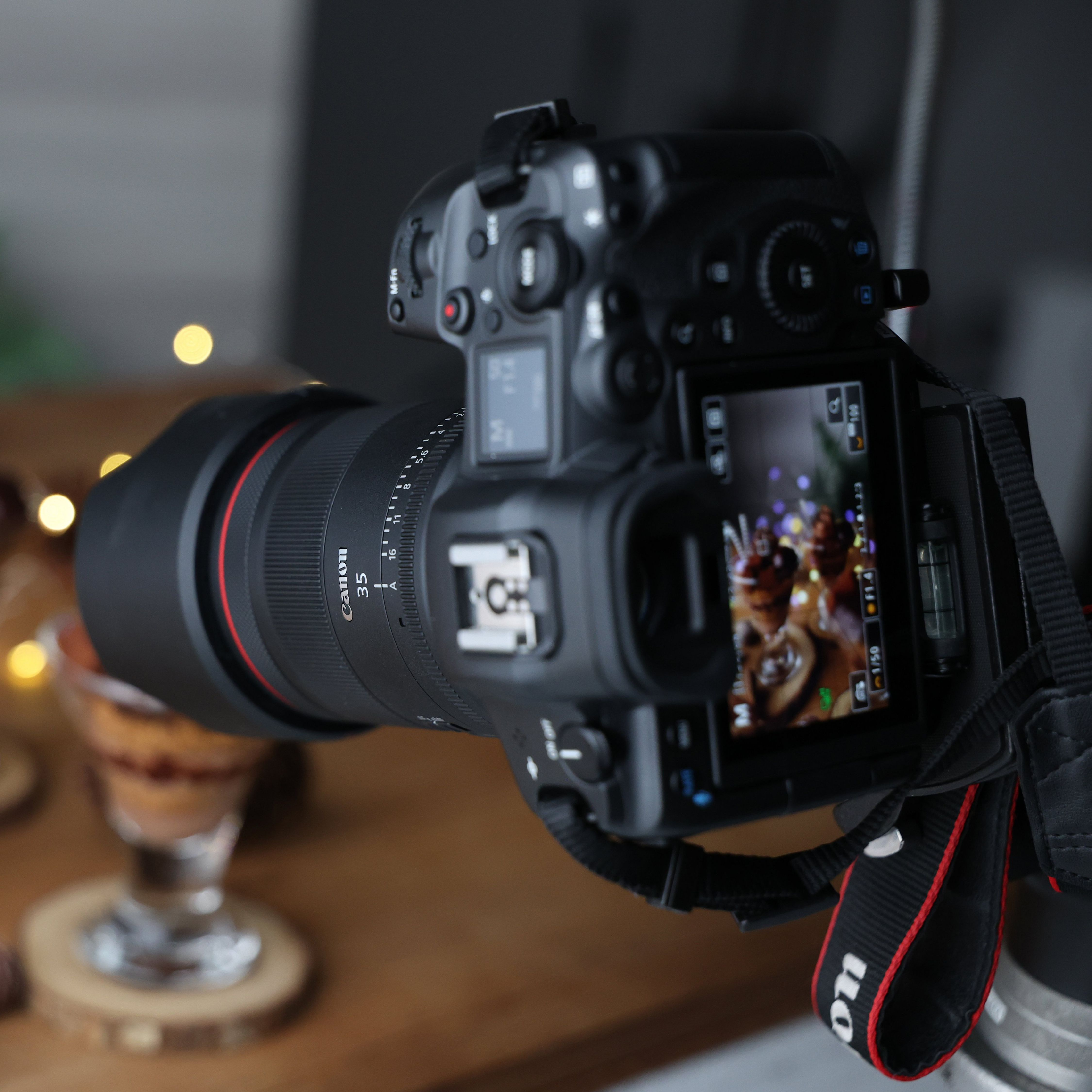 Un appareil photo Canon avec un objectif est installé. L'écran affiche une image floue. Une sangle dit Canon. L'arrière-plan a des lumières bokeh.