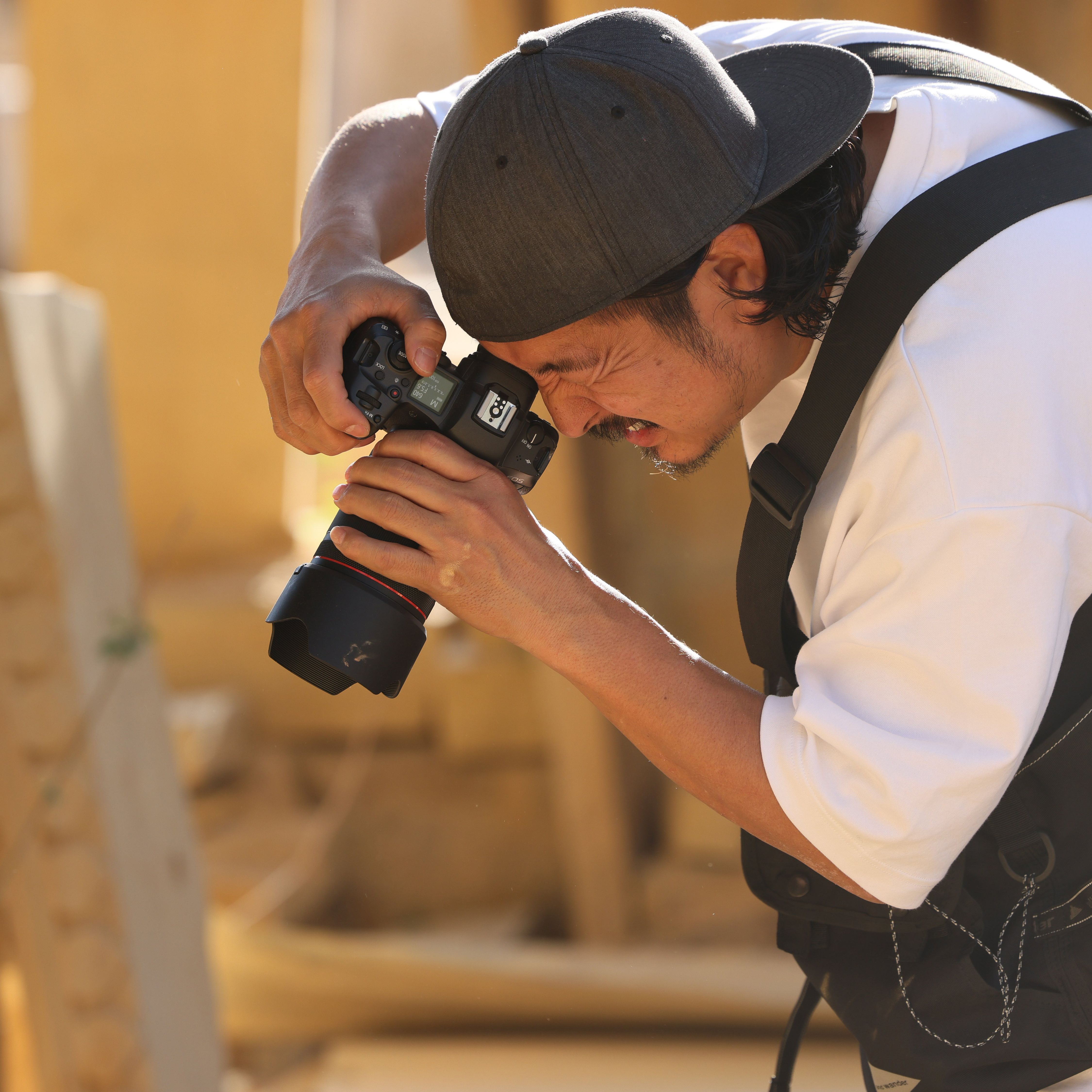Un homme portant une casquette et une chemise blanche prend une photo avec un appareil photo. Il plisse les yeux, concentré.