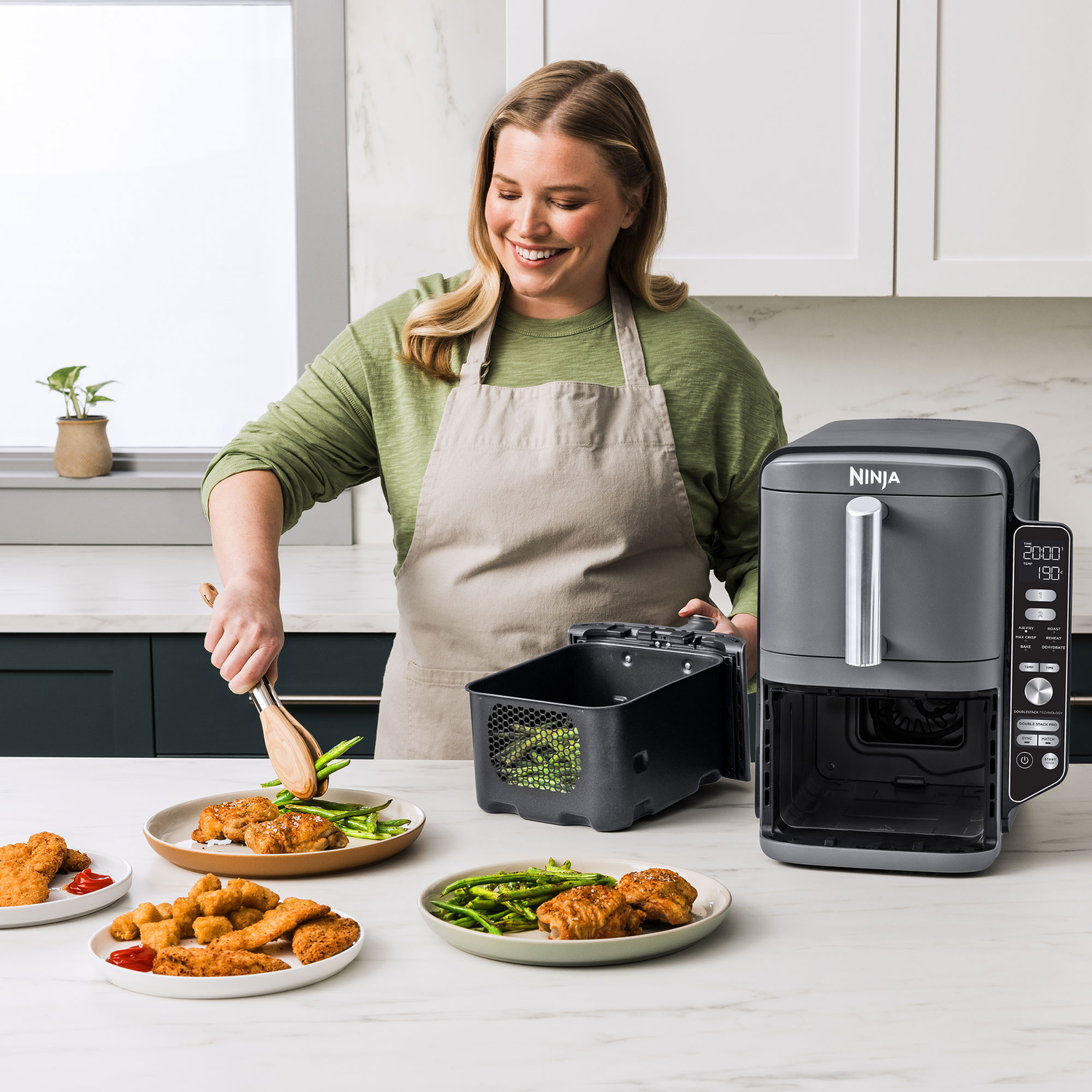 A woman preparing food with a Ninja air fryer, including chicken and vegetables.
