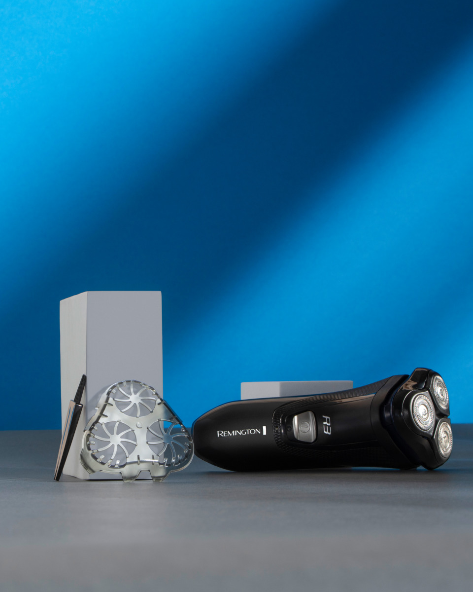 Rasoio elettrico Remington con testina di ricambio e supporto, su sfondo blu.