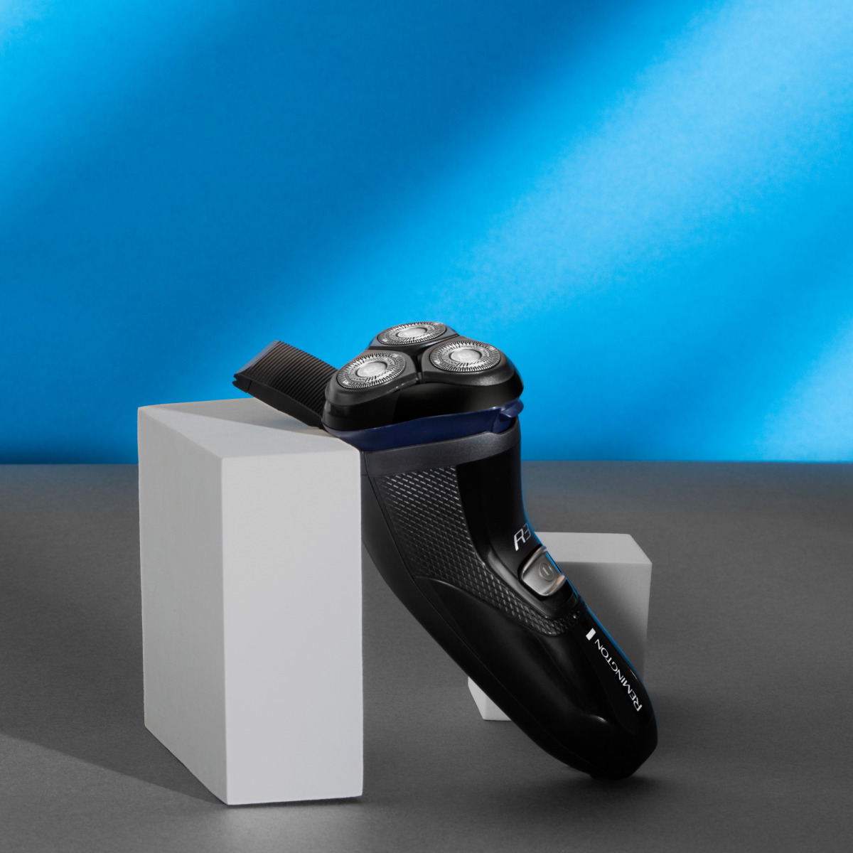 Rasoio Remington nero su blocchi bianchi con sfondo blu e grigio.