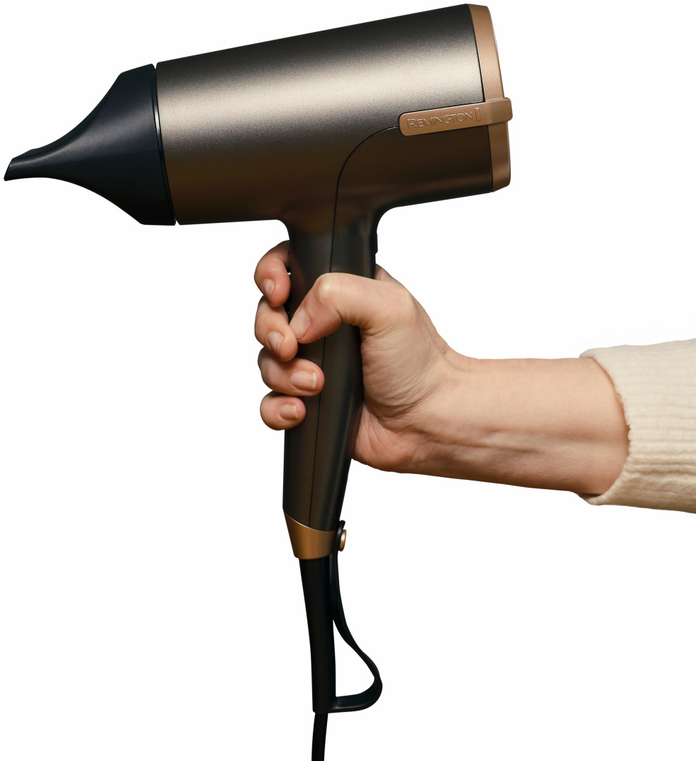 Una mano tiene un asciugacapelli Remington bronzo e nero su sfondo bianco.