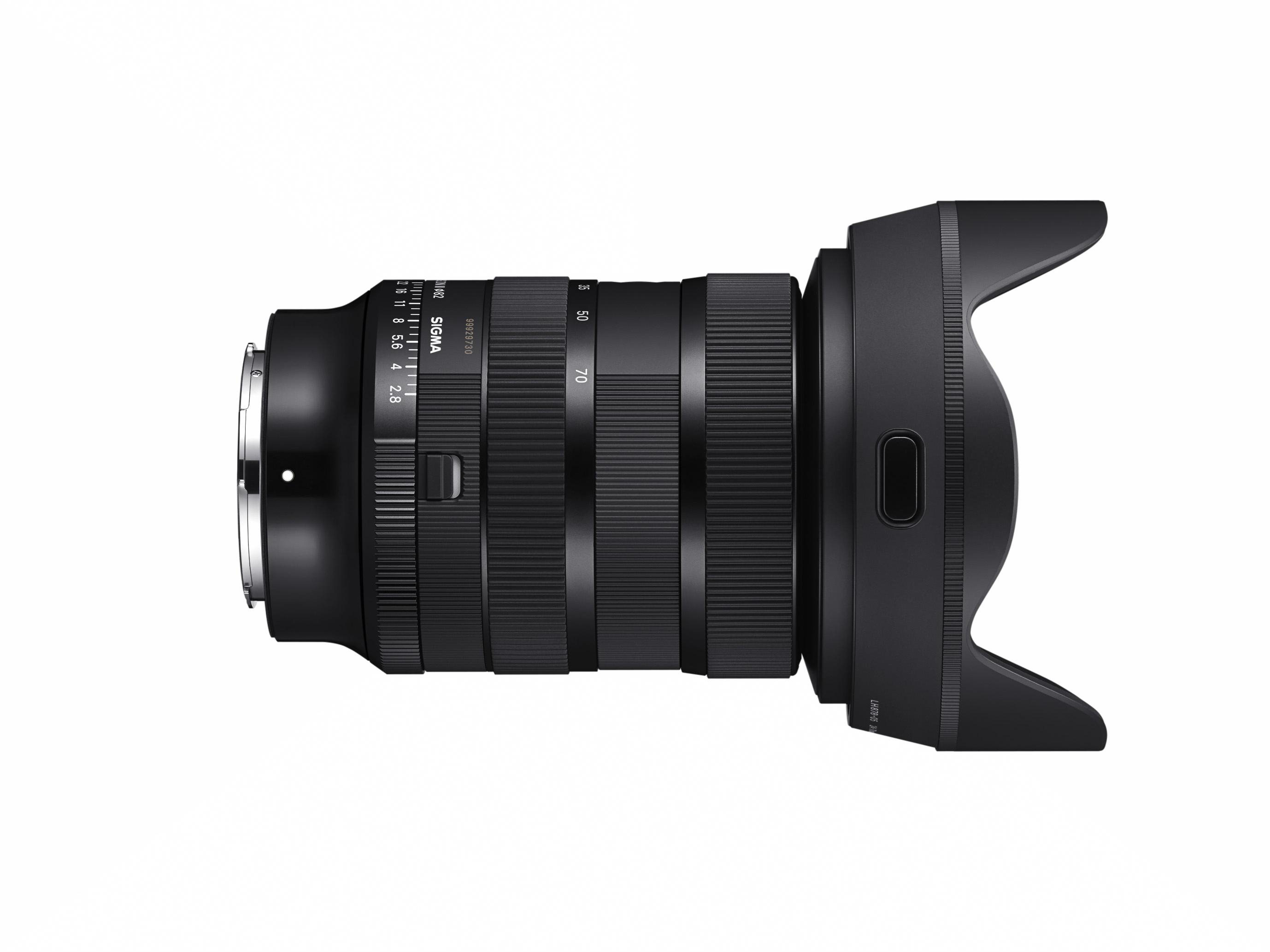 Ein schwarzes Sigma-Objektiv mit Sonnenblende, das auf einer weißen Oberfläche liegt.
