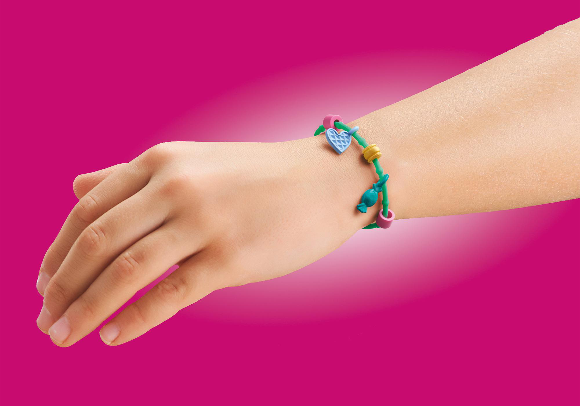 Hand mit buntem Armband mit Anhängern auf pinkem Hintergrund. Armband ist grün und blau.