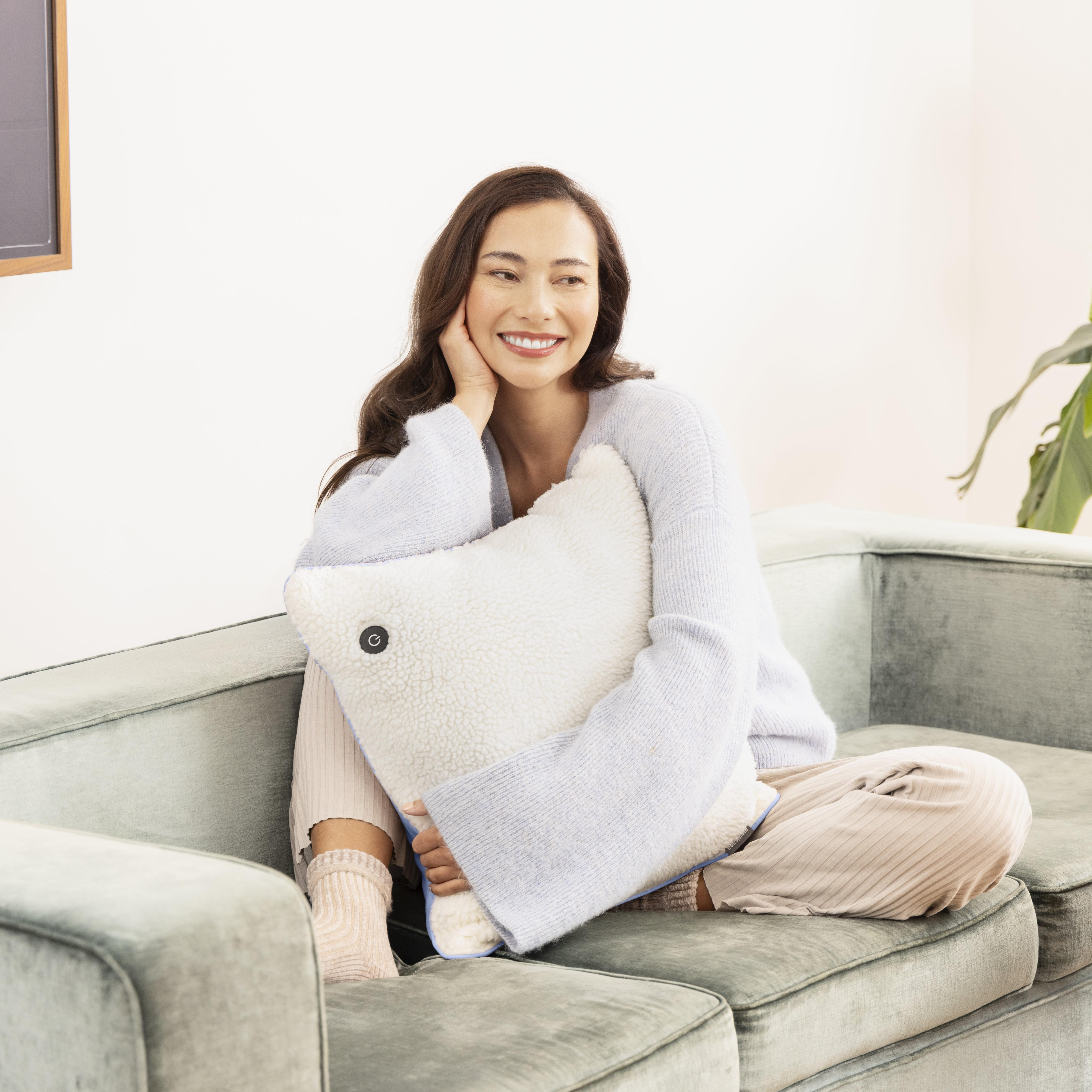 Frau mit Kissen sitzt auf Sofa, lächelt.