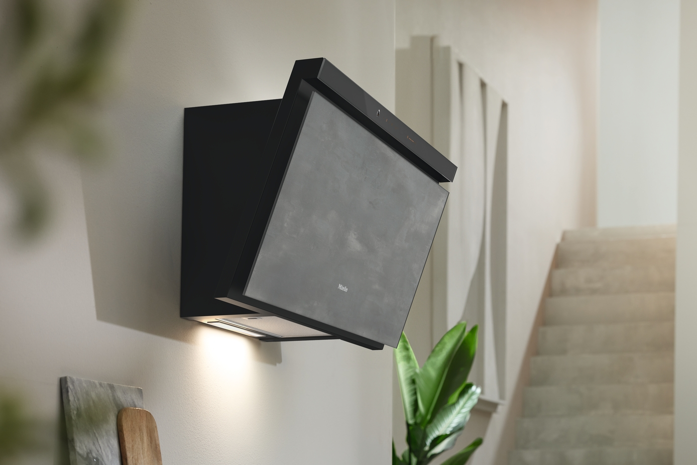 Schwarze Dunstabzugshaube an einer Wand montiert, mit Beleuchtung und Pflanzen.