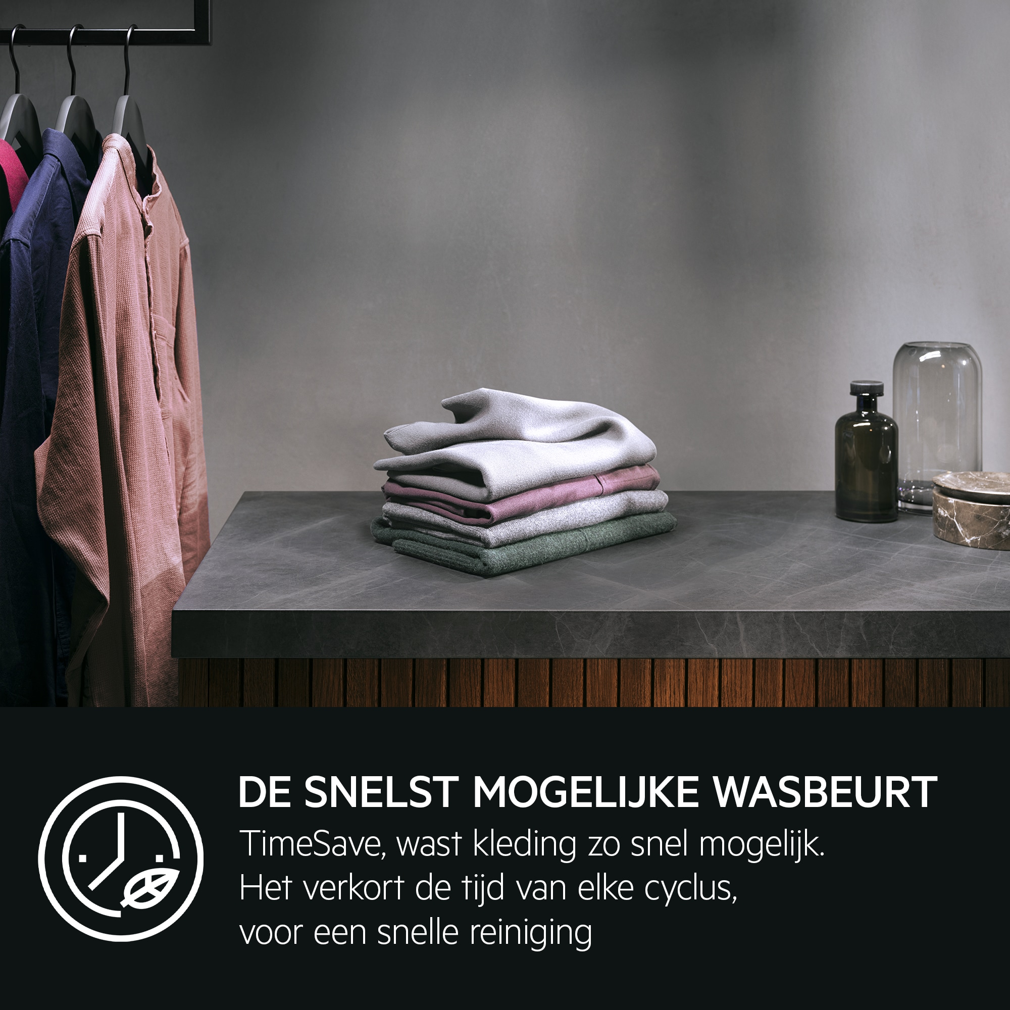 Clothes hanging on a rack, with a stack of folded towels on a counter.