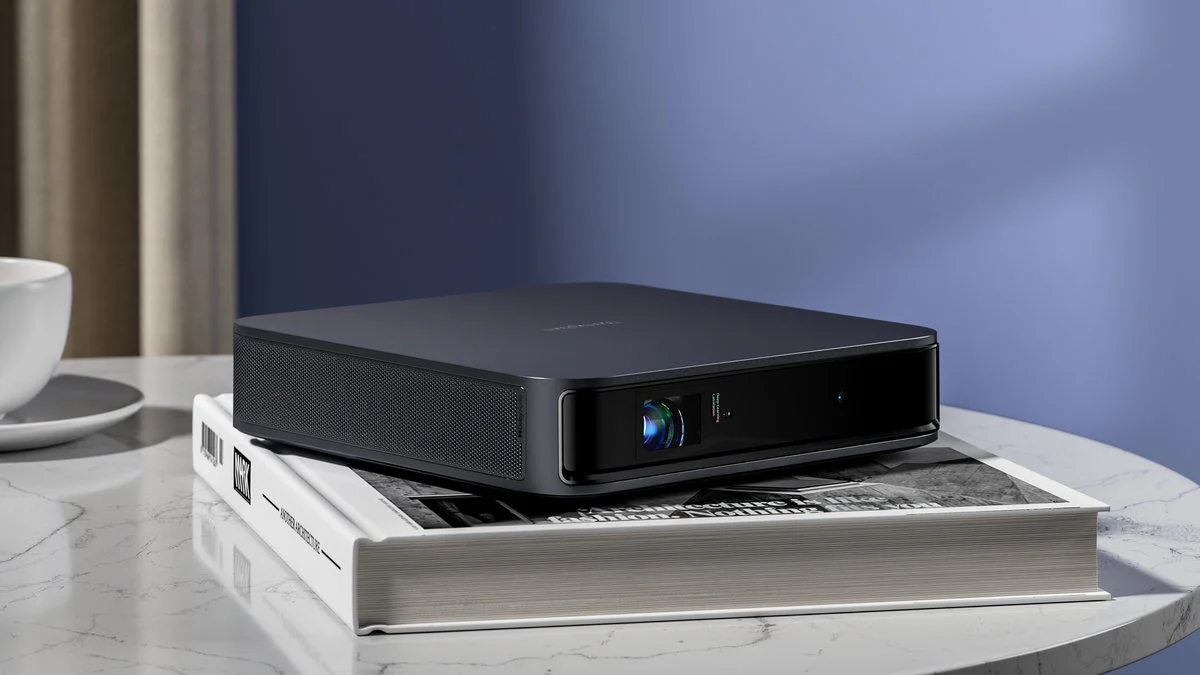 Czarny projektor na białej książce, umieszczony na białym stole. Niebieska ściana w tle.