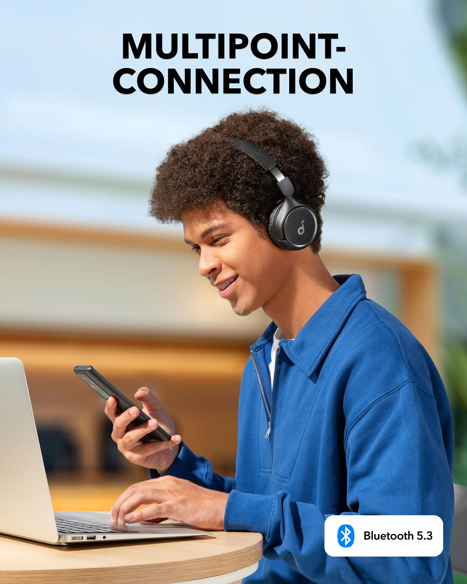 Mann benutzt Laptop und Smartphone mit Kopfhörern. Anker-Logo sichtbar.