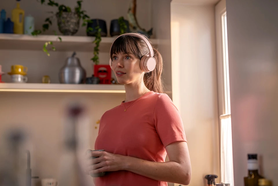 Kobieta w różowych słuchawkach patrzy w lewo, trzymając filiżankę.