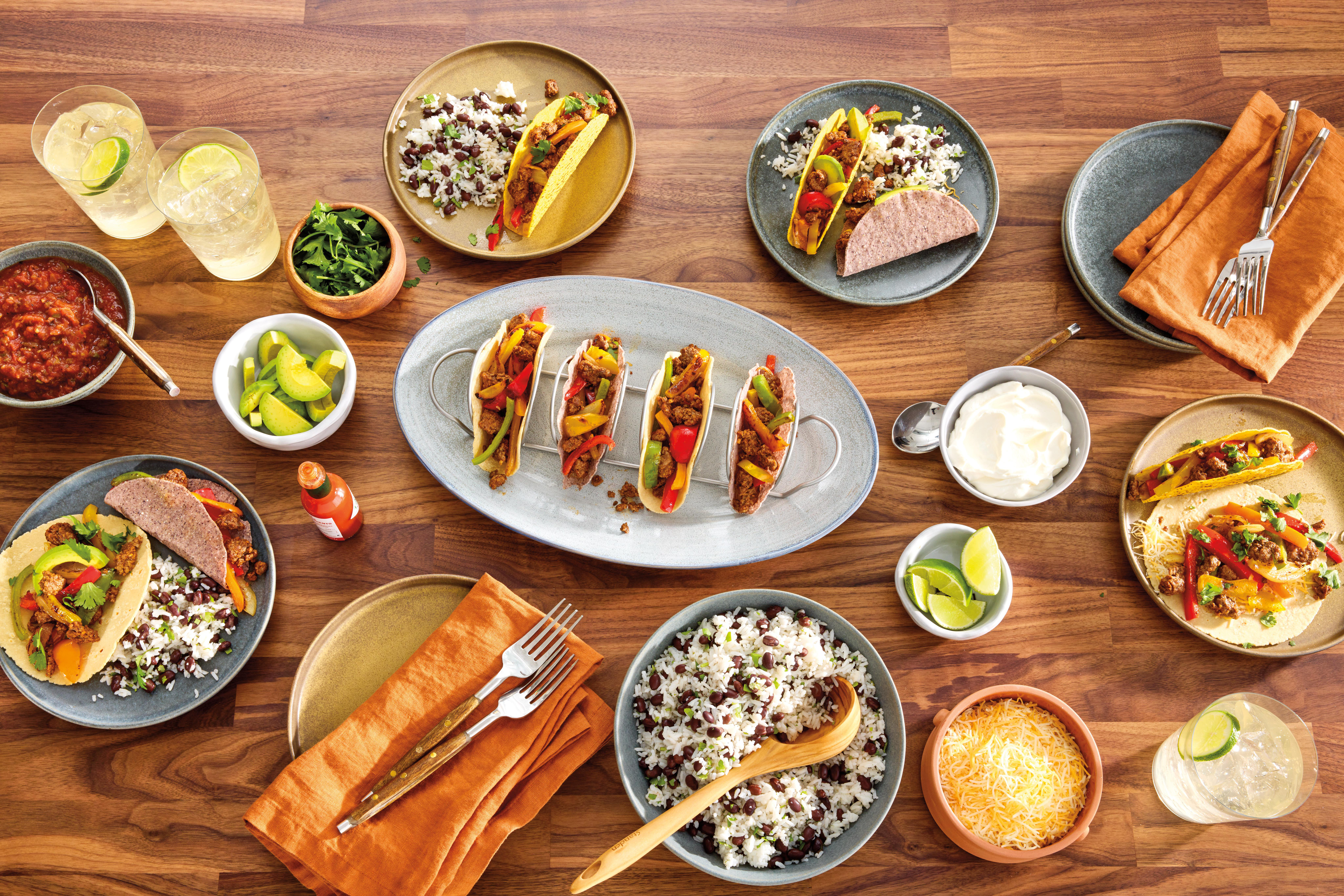 Ein Holztisch mit Tacos, Reis, Getränken und Gewürzen.