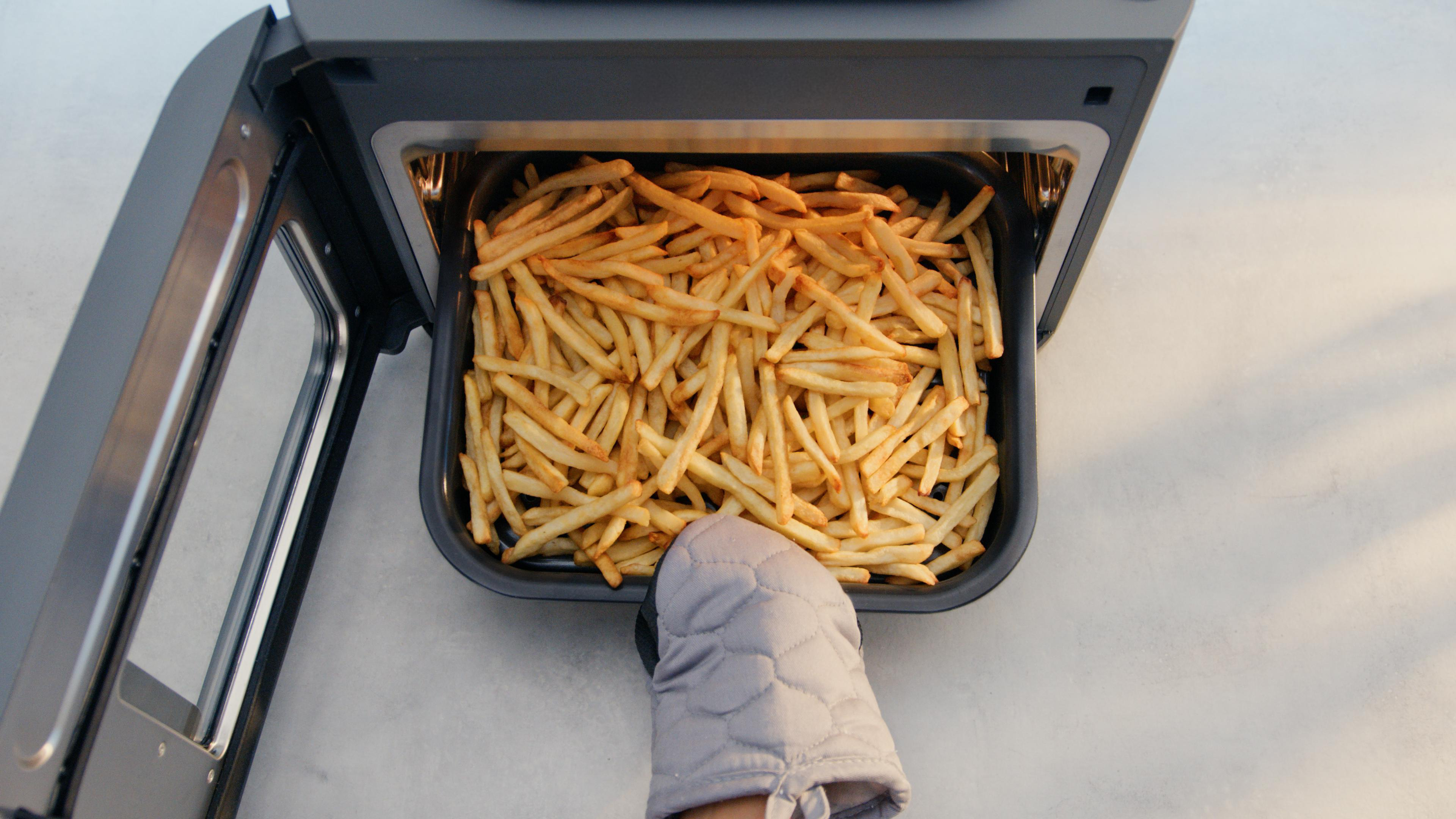 Luftfritteusen-Schublade gefüllt mit frittierten Pommes Frites und einem Handschuh daneben.