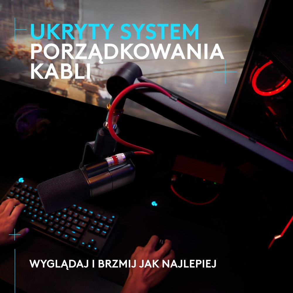 Zbliżenie mikrofonu z czerwonym ramieniem, klawiaturą i monitorem. Scena jest ciemna.