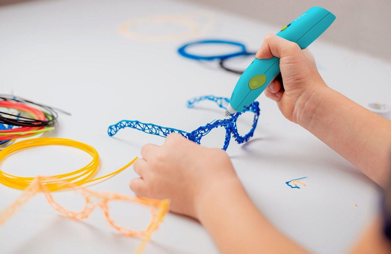 Eine Person verwendet einen 3D-Stift, um eine blaue Brille auf einer weißen Oberfläche zu erstellen.