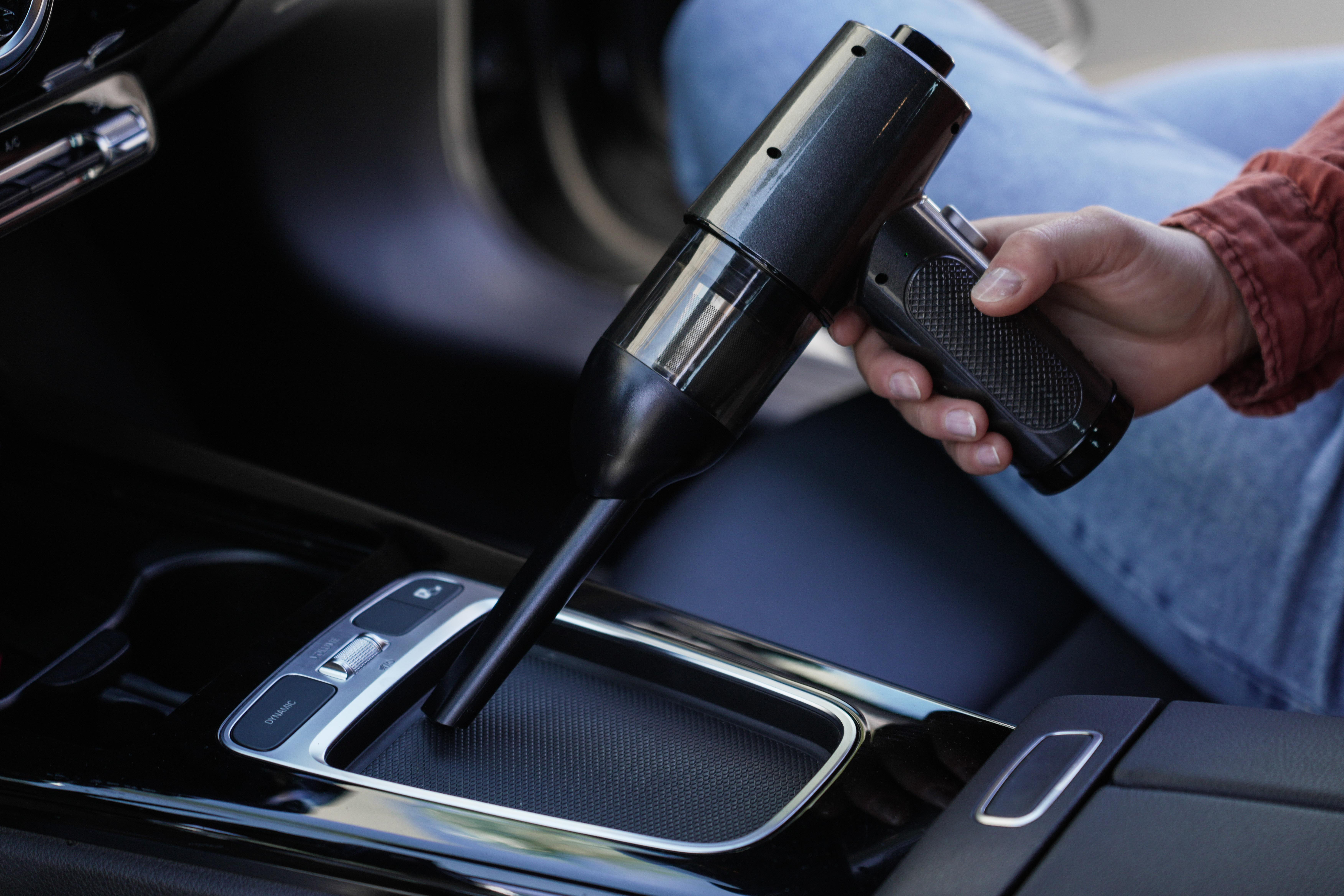 Hand hält schwarzen Autostaubsauger, reinigt das Auto, schwarze Konsole.