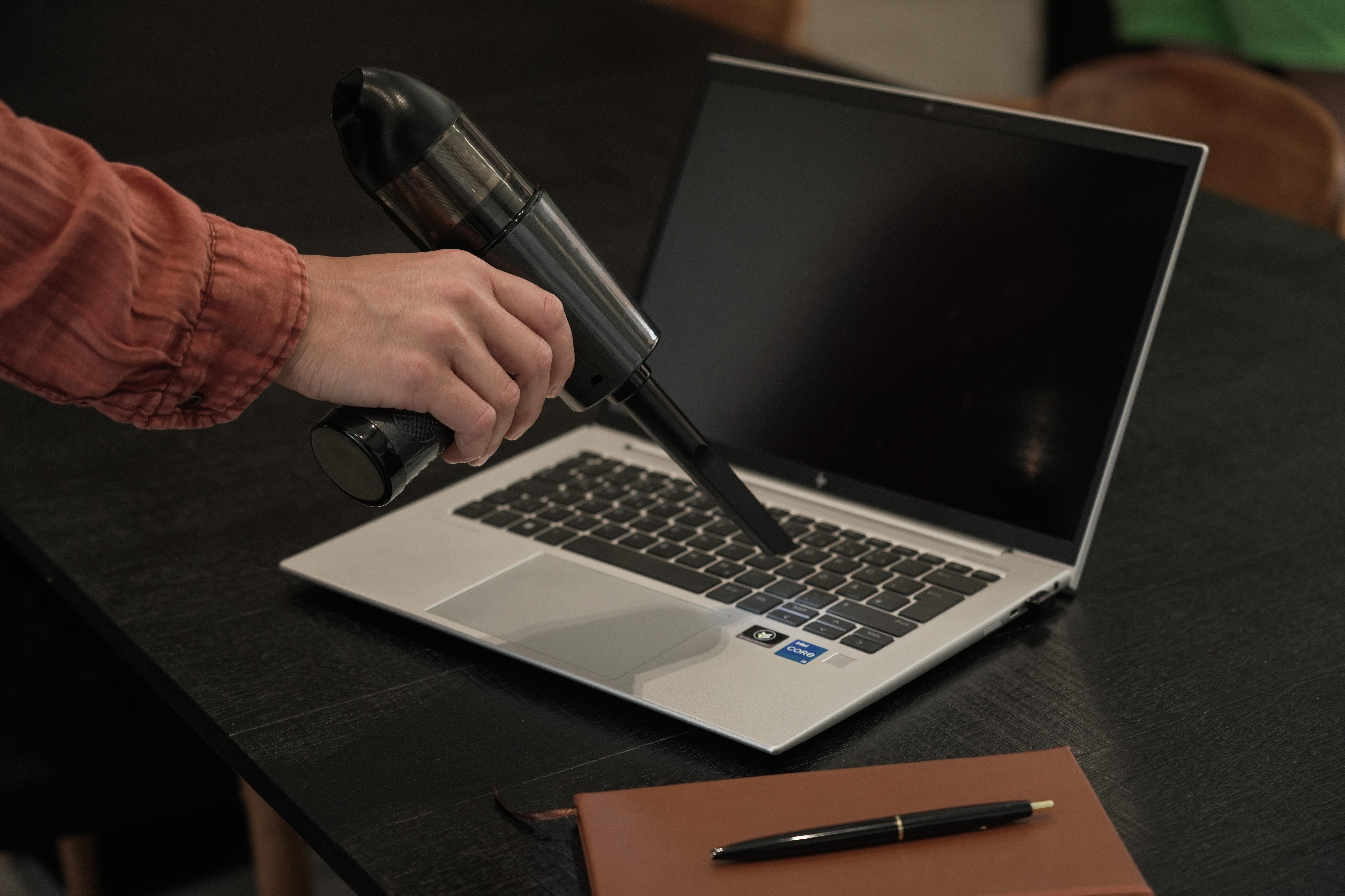 Eine Person, die eine Laptop-Tastatur mit einem Handstaubsauger absaugt.