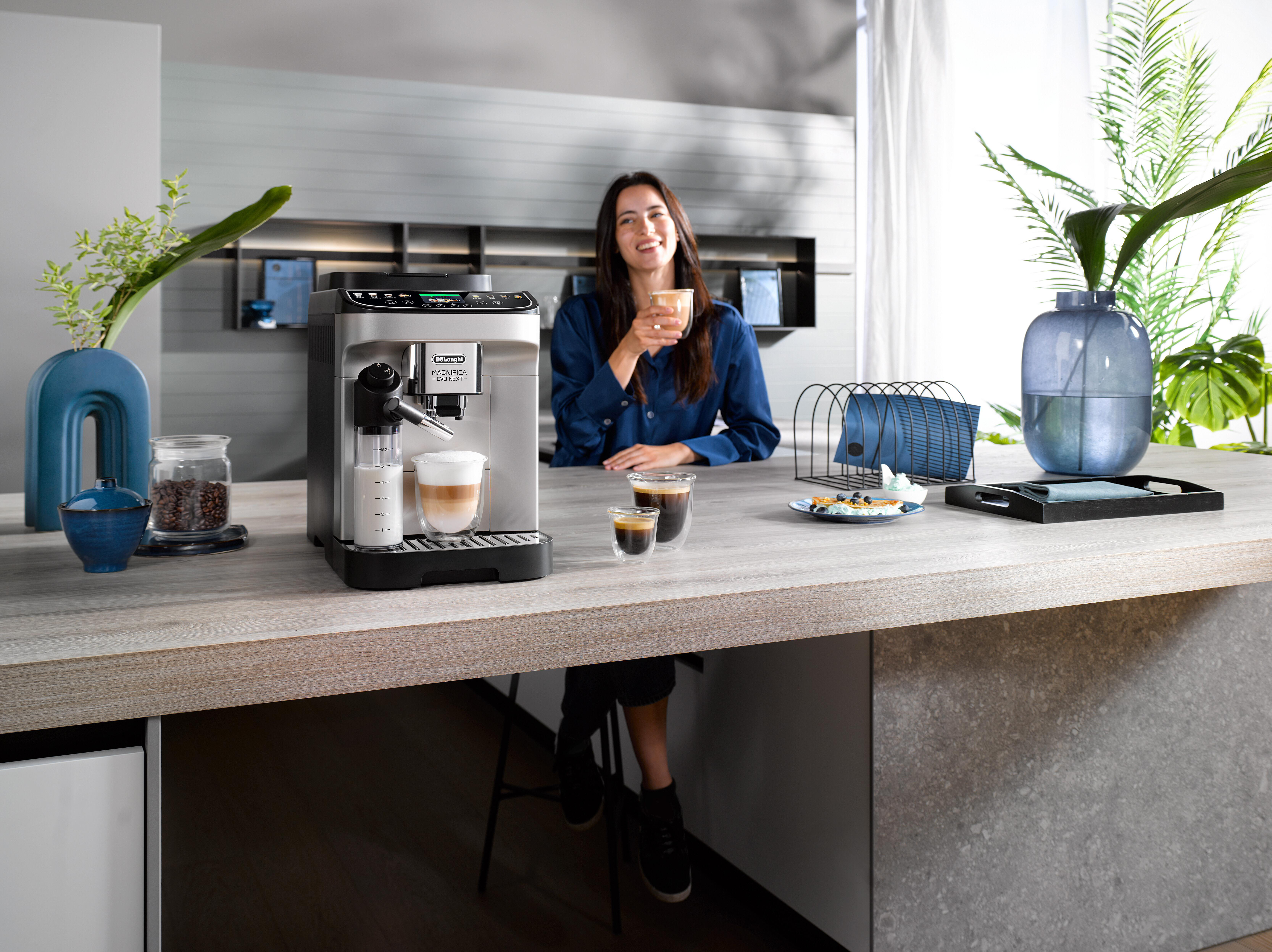 Frau lächelt, hält eine Tasse, neben einer Kaffeemaschine, verschiedene Objekte.