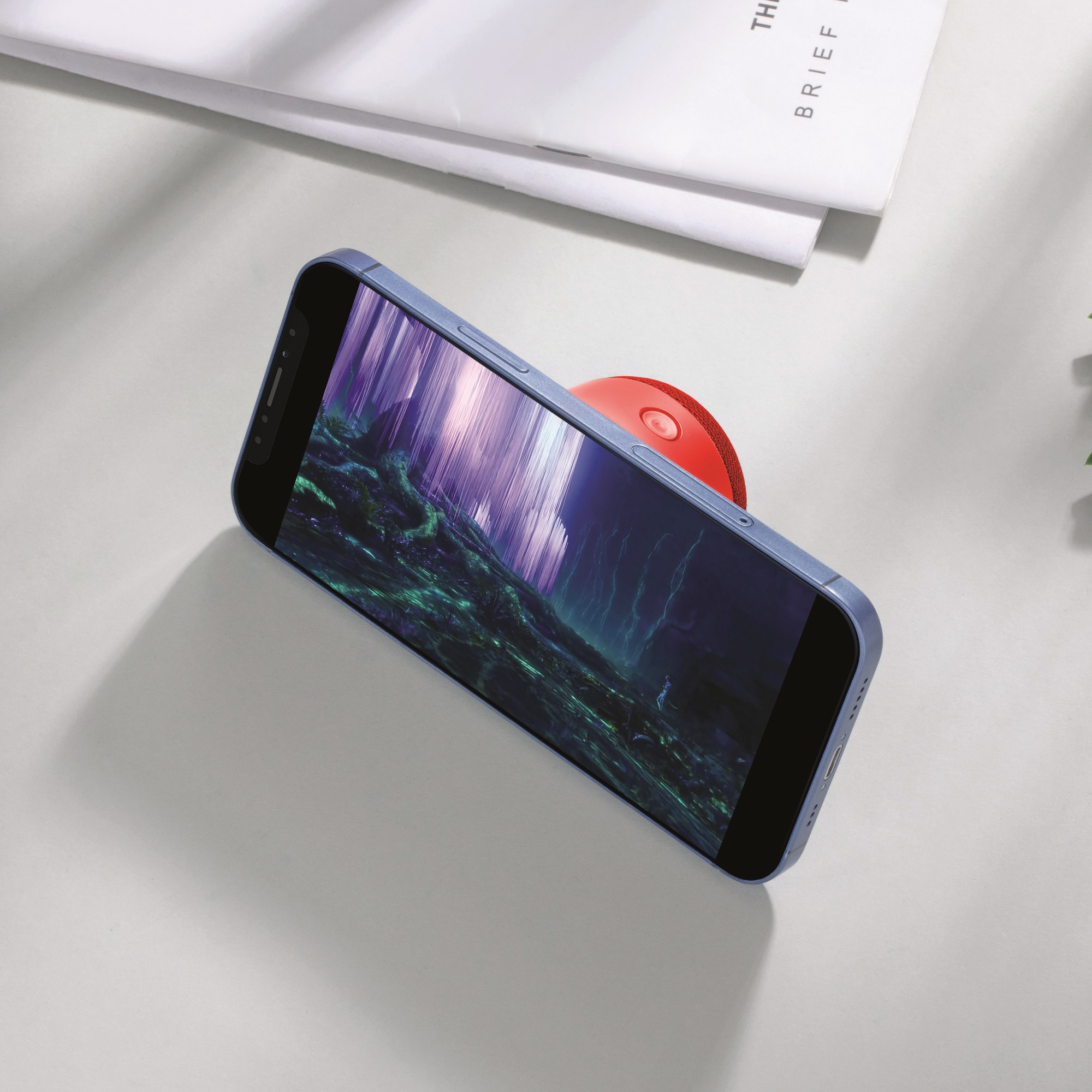 Ein blaues Telefon mit rotem Pop-Socket auf weißer Oberfläche neben einer Zeitschrift.