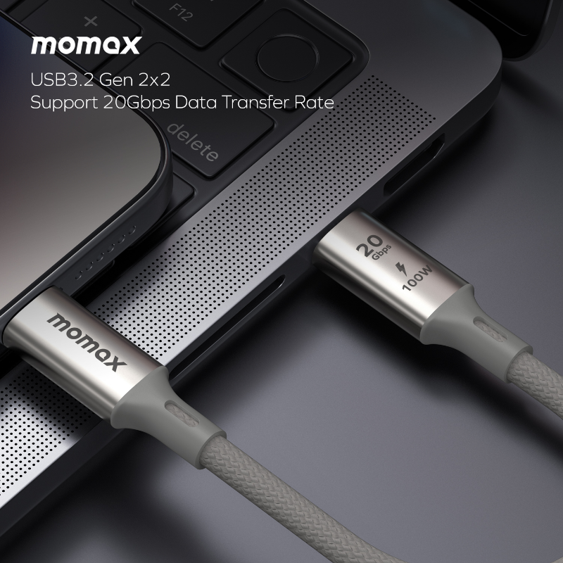 USB-C kablosu takılı bir dizüstü bilgisayar. Kablo gri ve üzerinde momax yazısı var.