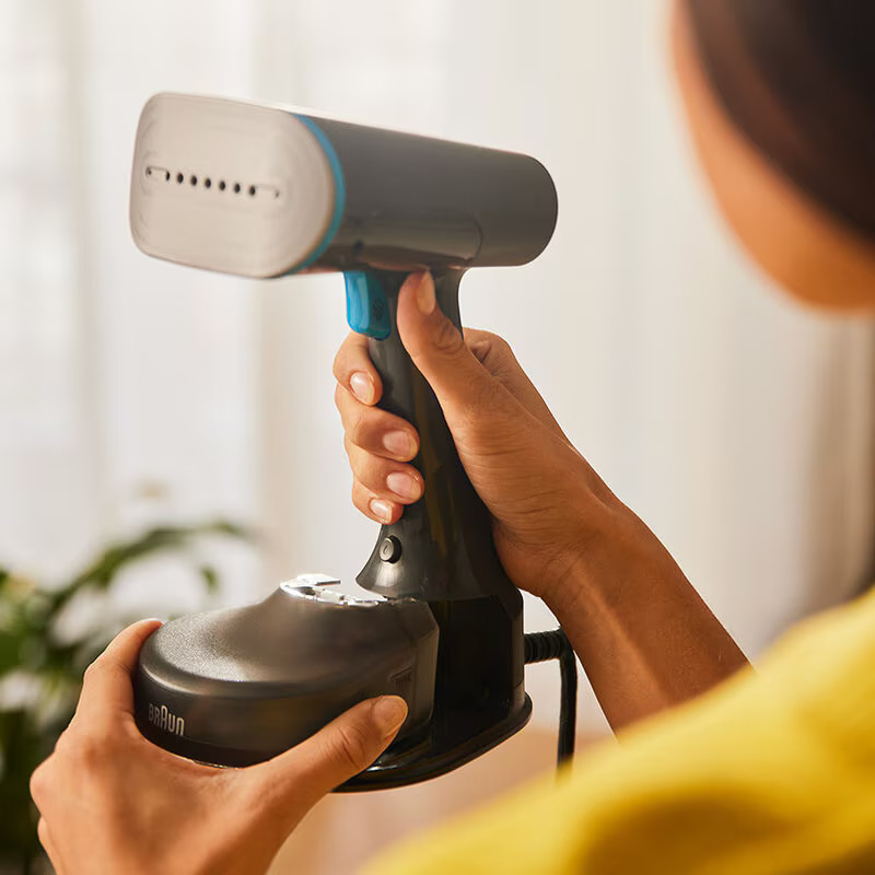 Osoba trzymająca czarno-niebieską parownicę do ubrań, zbliżenie na szczegóły.