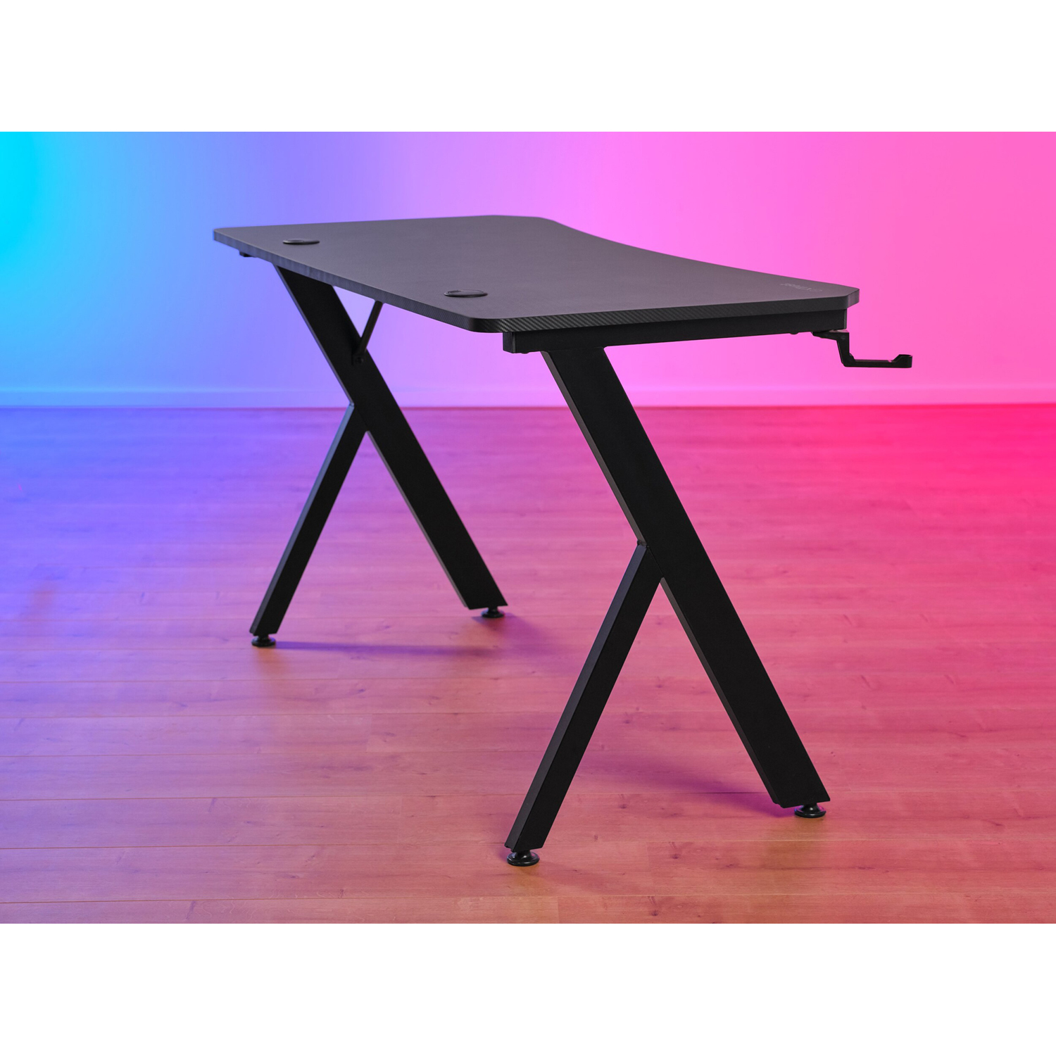 Scrivania da gioco nera con piano inclinato e gambe a X su pavimento in legno, sfondo sfumato.