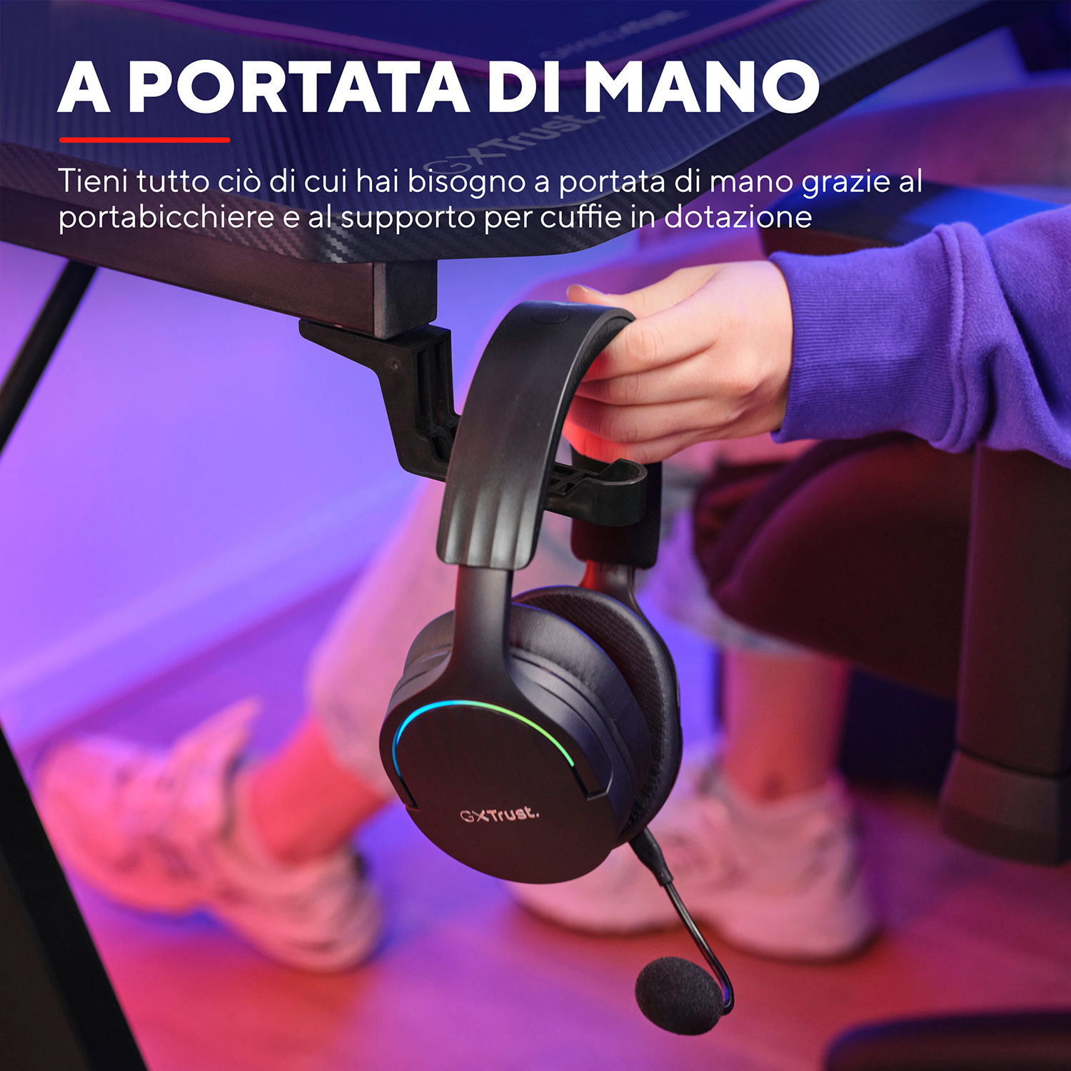 Cuffie appese a una scrivania. Una mano tiene le cuffie. La scrivania ha un portabicchieri.