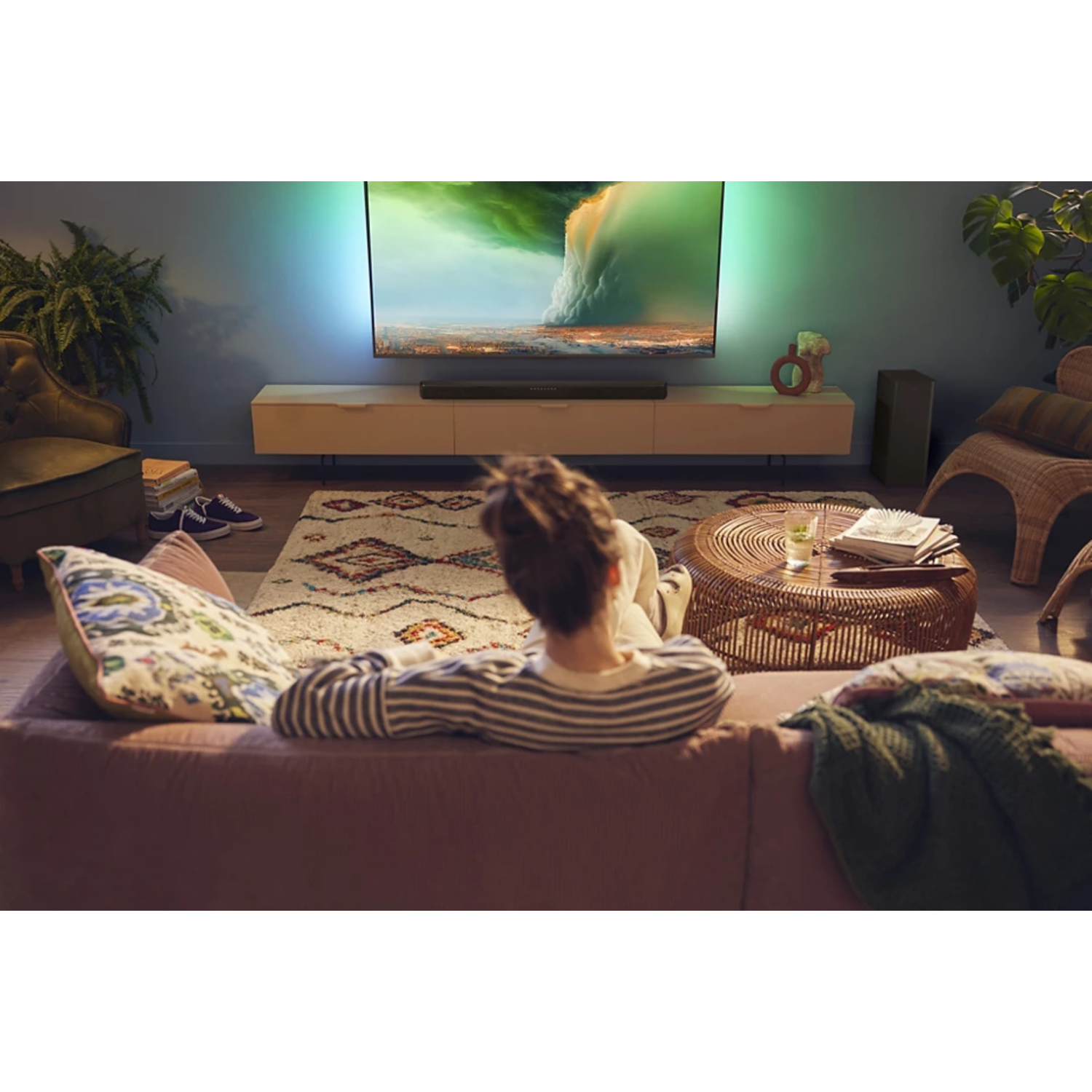 Une personne assise sur un canapé regarde la télévision. La pièce est bien éclairée et de design moderne.