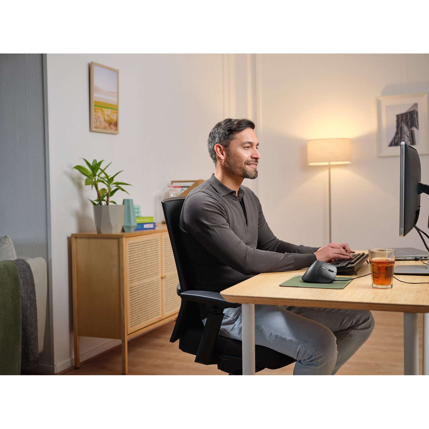 Uomo usa computer a scrivania. C'è una pianta, una tazza e una lampada.