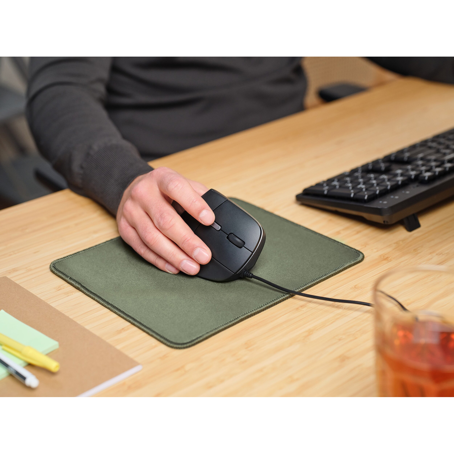 Mano che tiene un mouse nero su un tappetino verde.