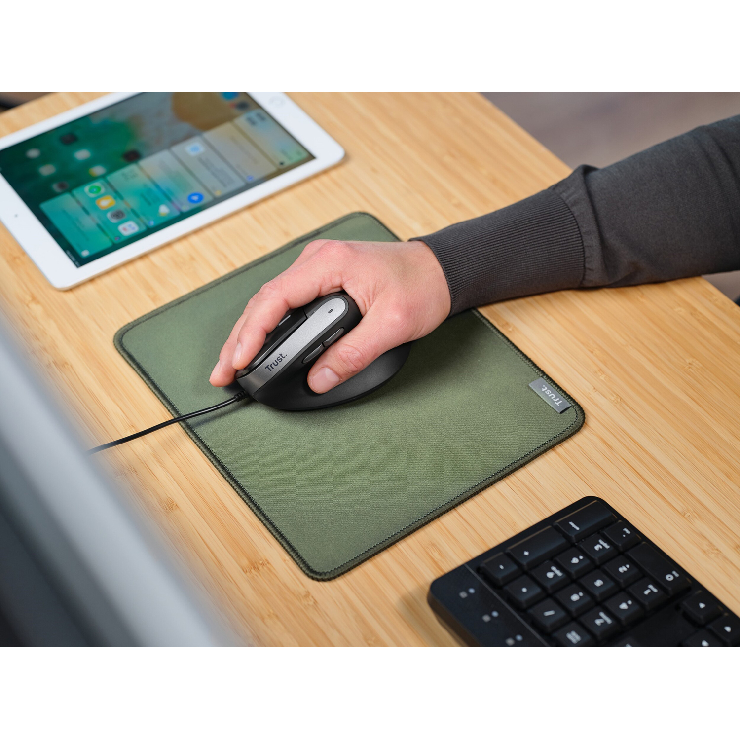 Una mano usa un mouse nero su un tappetino verde, accanto a un tablet e una tastiera.
