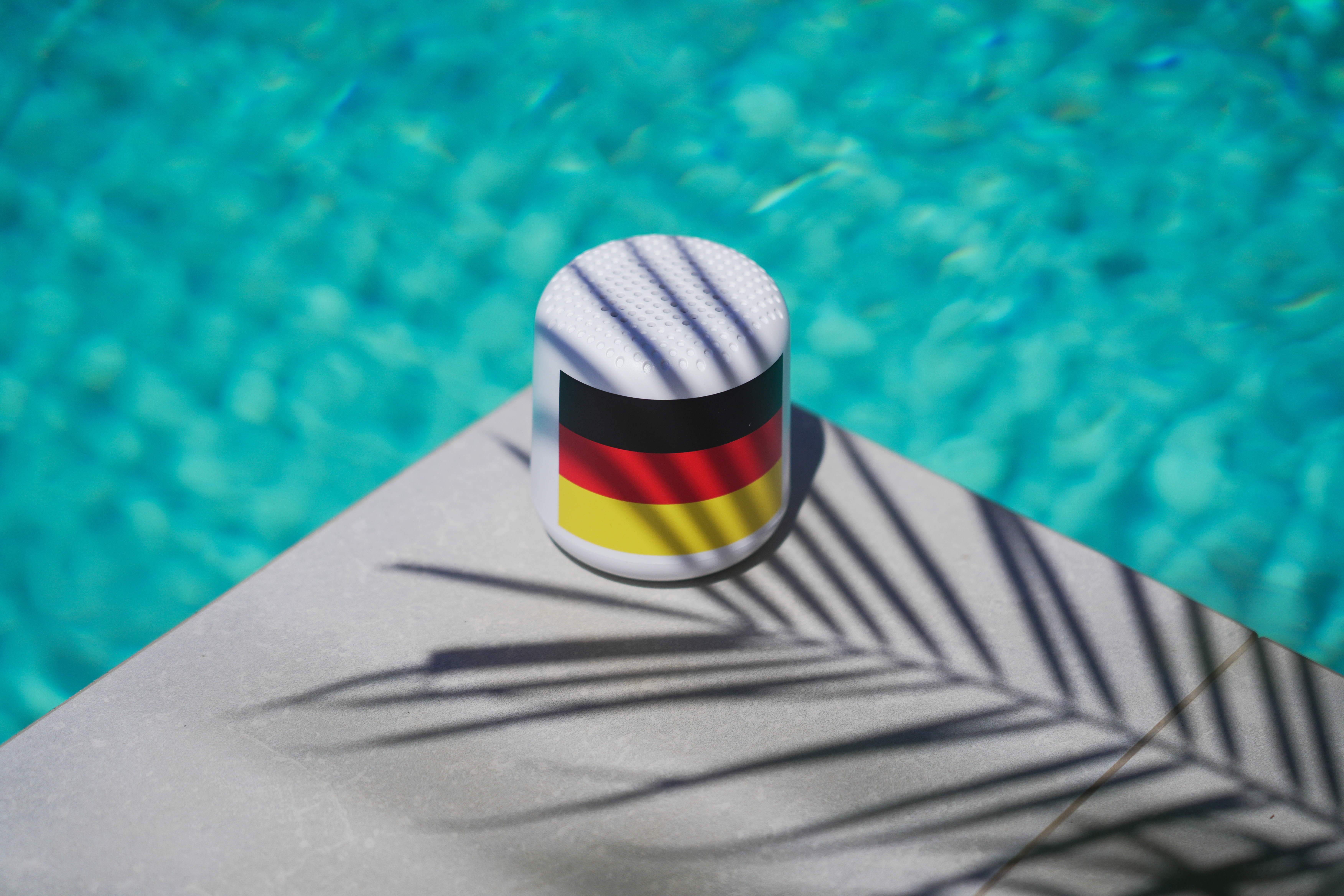 Weißer Lautsprecher mit deutschen Flaggenfarben, auf grauer Steinoberfläche.
