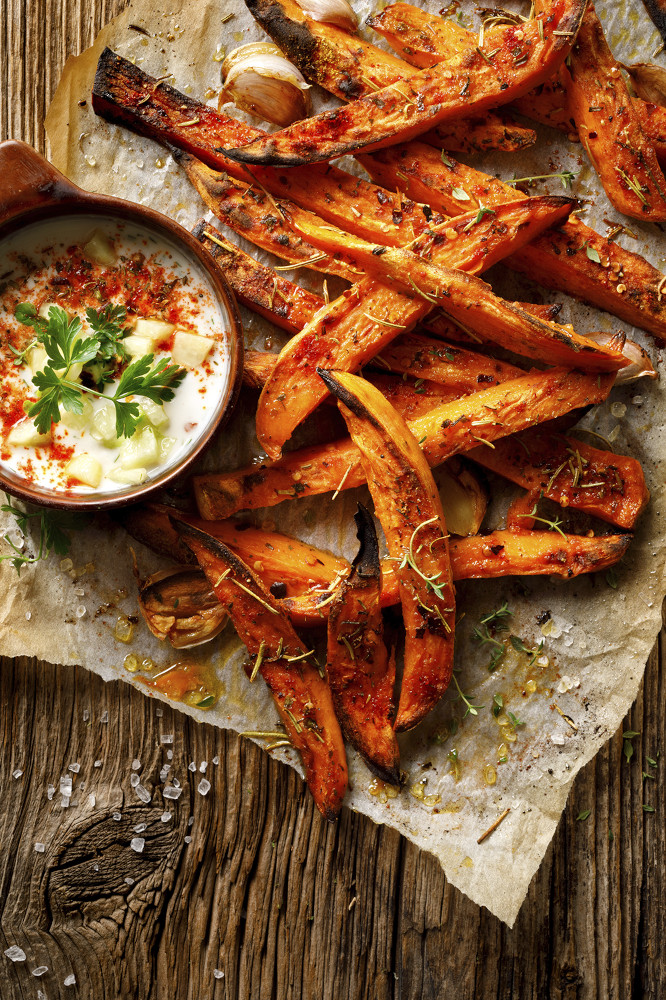 Overhead shot of sweet potato fries and a bowl of dipping sauce on a wooden table.