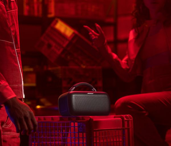 Czarny głośnik Bose na czerwonej skrzyni, z ludźmi w czerwono oświetlonym pokoju.