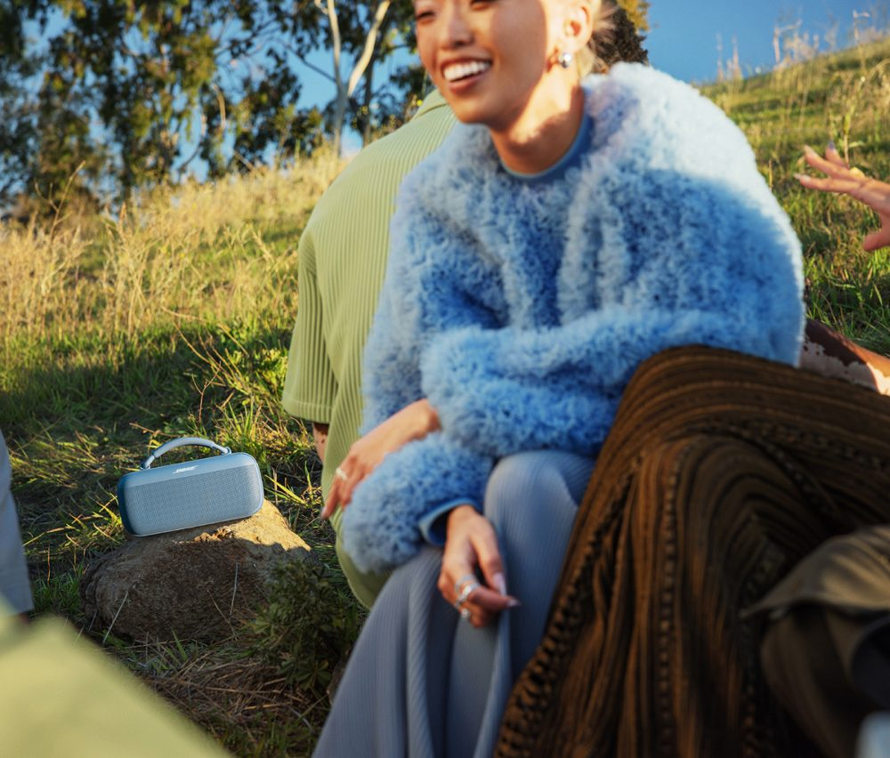 Grupa ludzi na zewnątrz z niebieskim głośnikiem. Głośnik stoi na skale. Widoczne jest niebo.