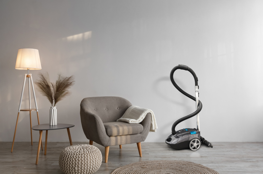 A living room with a grey armchair, floor lamp, and vacuum cleaner.