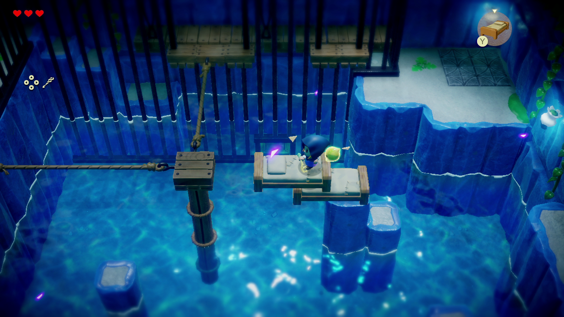 Una scena di dungeon illuminata di blu da un videogioco. Un personaggio è in piedi su un letto, l'acqua lo circonda.