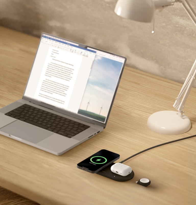 Laptop töltő telefonnal, vezeték nélküli fülhallgatóval és okosórával az asztalon.
