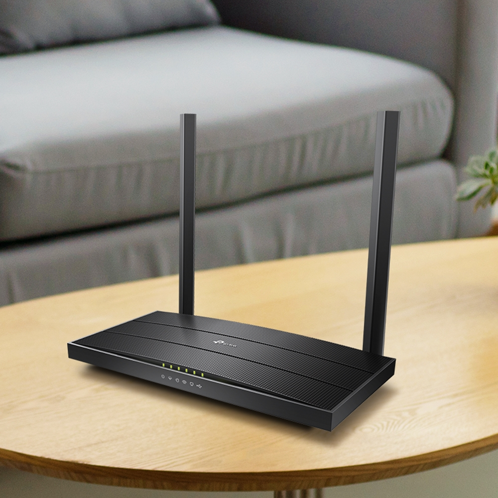 İki antenli siyah bir TP-Link yönlendirici, ahşap bir masaya yerleştirilmiş. Arka planda gri bir kanepe.