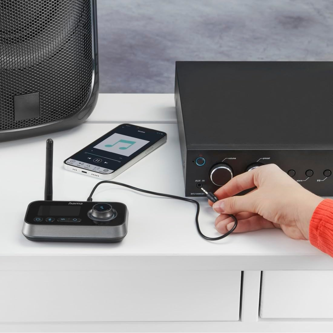 Un receptor de audio inalámbrico negro conectado a un teléfono inteligente y un amplificador negro sobre una mesa blanca.