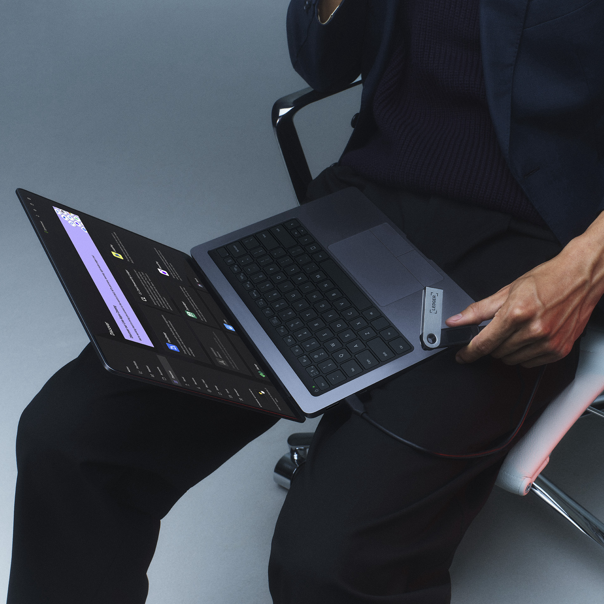 Bir kişi bir dizüstü bilgisayar ve bir Ledger cihazı tutuyor. Dizüstü bilgisayar açık, bir web sitesi görüntülüyor.