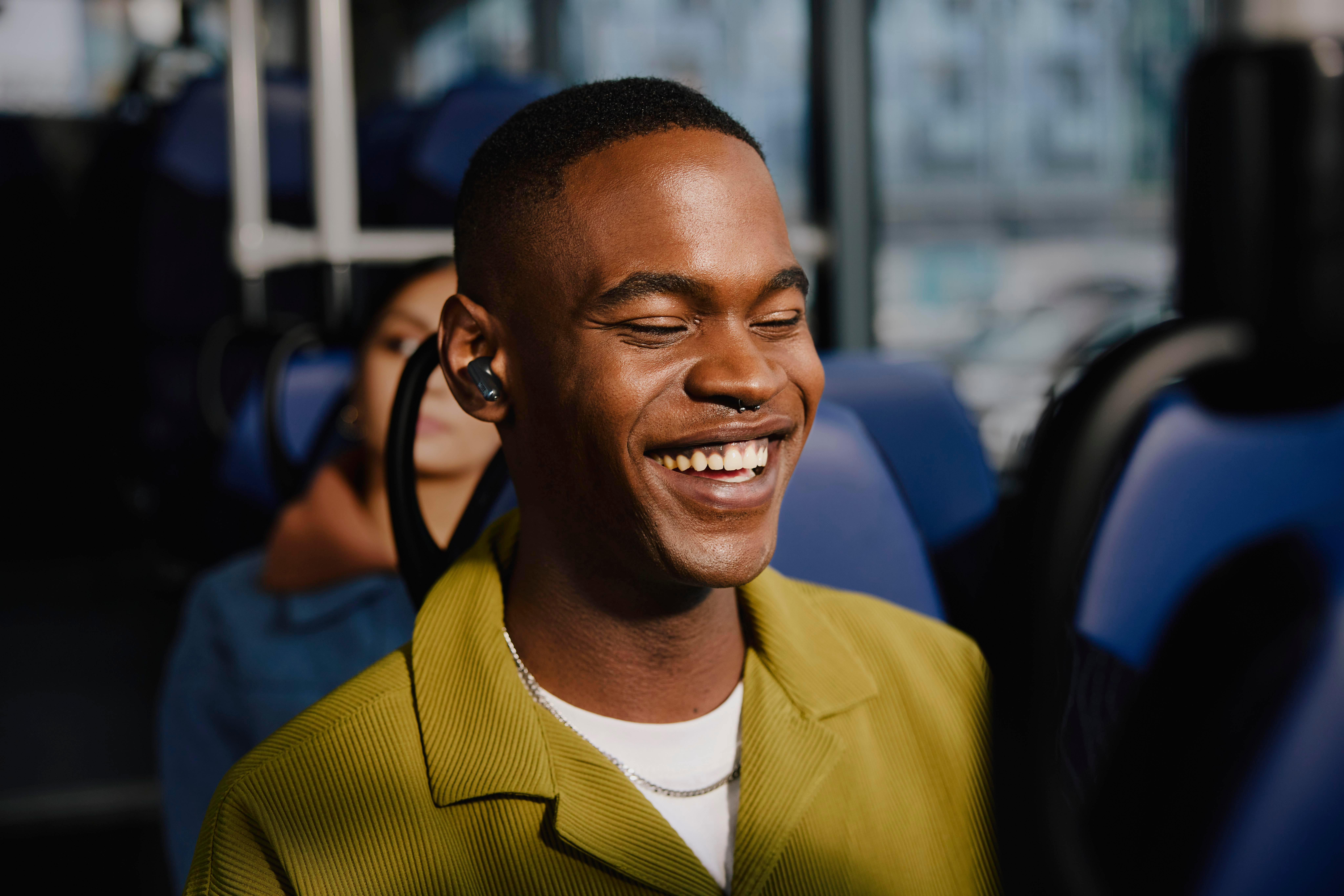 Glücklicher schwarzer Mann im Bus, trägt Ohrhörer und gelbe Jacke. Er lächelt.