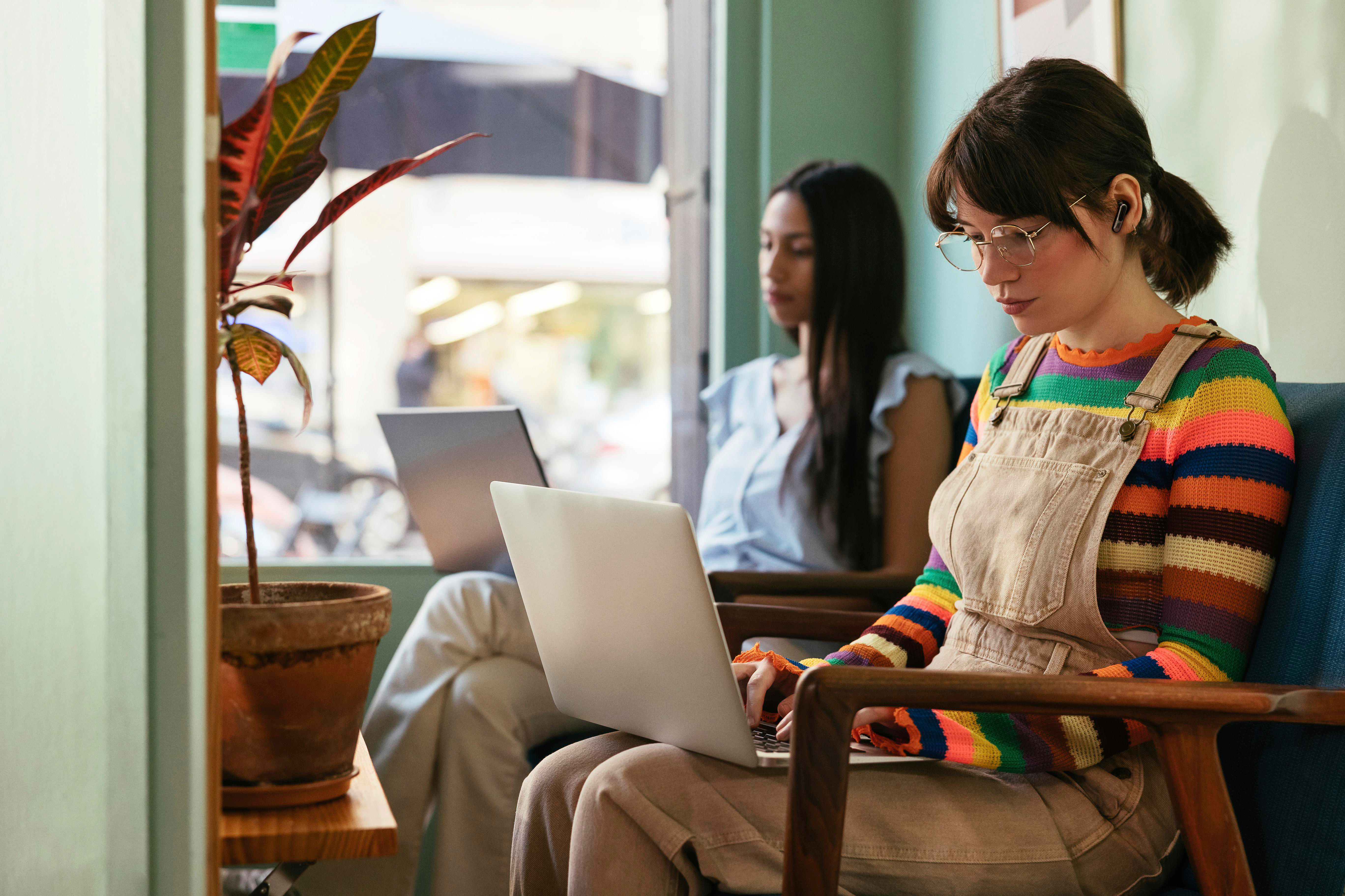 Zwei Frauen arbeiten in einem gut beleuchteten Raum an Laptops.