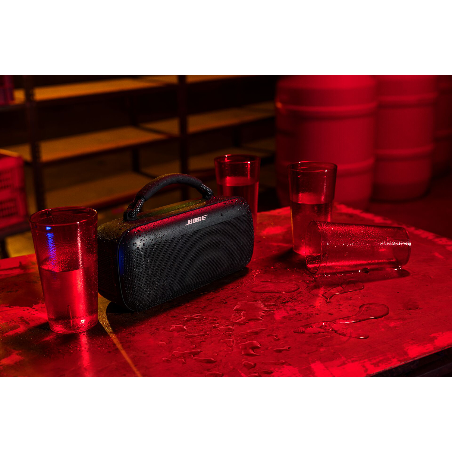 Un altoparlante Bose nero, con tre bicchieri d'acqua e illuminazione rossa.